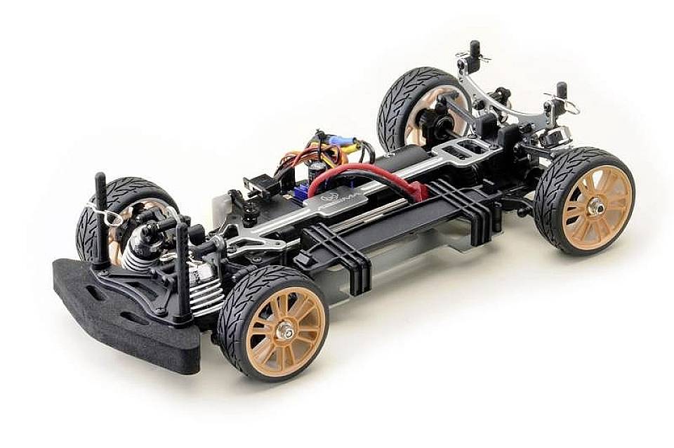 Ein offene Chassis eines ferngesteuerten Autos zeigt Räder, Federung und Elektronikkomponenten auf einer weißen Oberfläche.