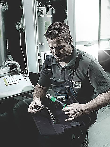 Ein Techniker in Arbeitskleidung, kniend, untersucht Teile mit Werkzeugen in der Nähe und führt höchstwahrscheinlich Wartungsarbeiten an industrieller Maschinerie durch.