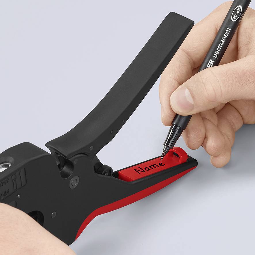 Eine Hand beschriftet mit einem schwarzen Stift ein rotes Namensschild, das in einem Gerät zum Erstellen von Etiketten eingespannt ist.