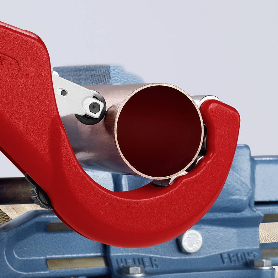 Rohrschneider schneidet ein Kupferrohr; Metallrohr ist in rote Klinge eingespannt. Hintergrund zeigt Werkbank und Werkzeug.