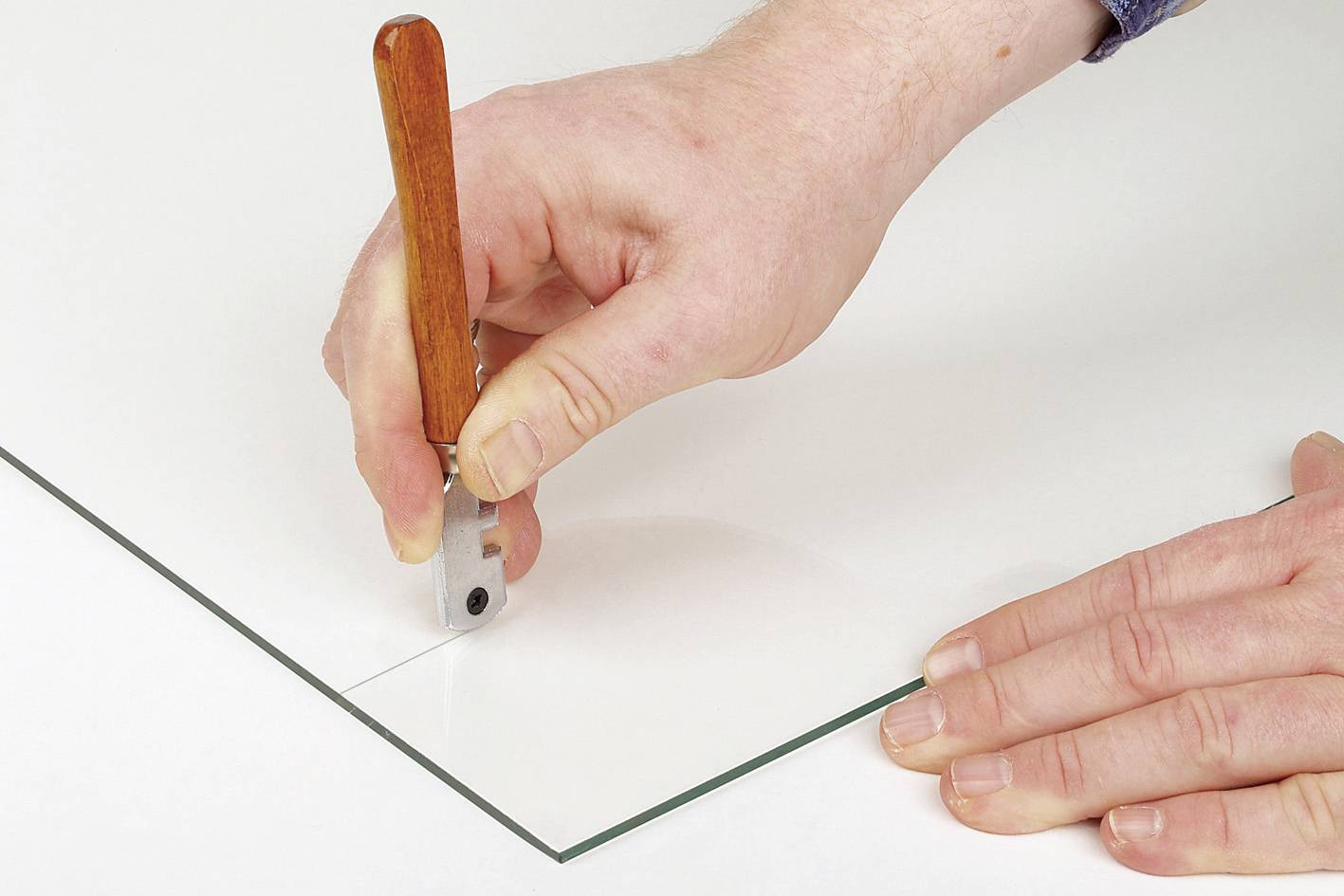 Eine Person schneidet eine Glasscheibe mit einem Glasschneider entlang einer geraden Linie. Hände sind sichtbar, keine weiteren Objekte.