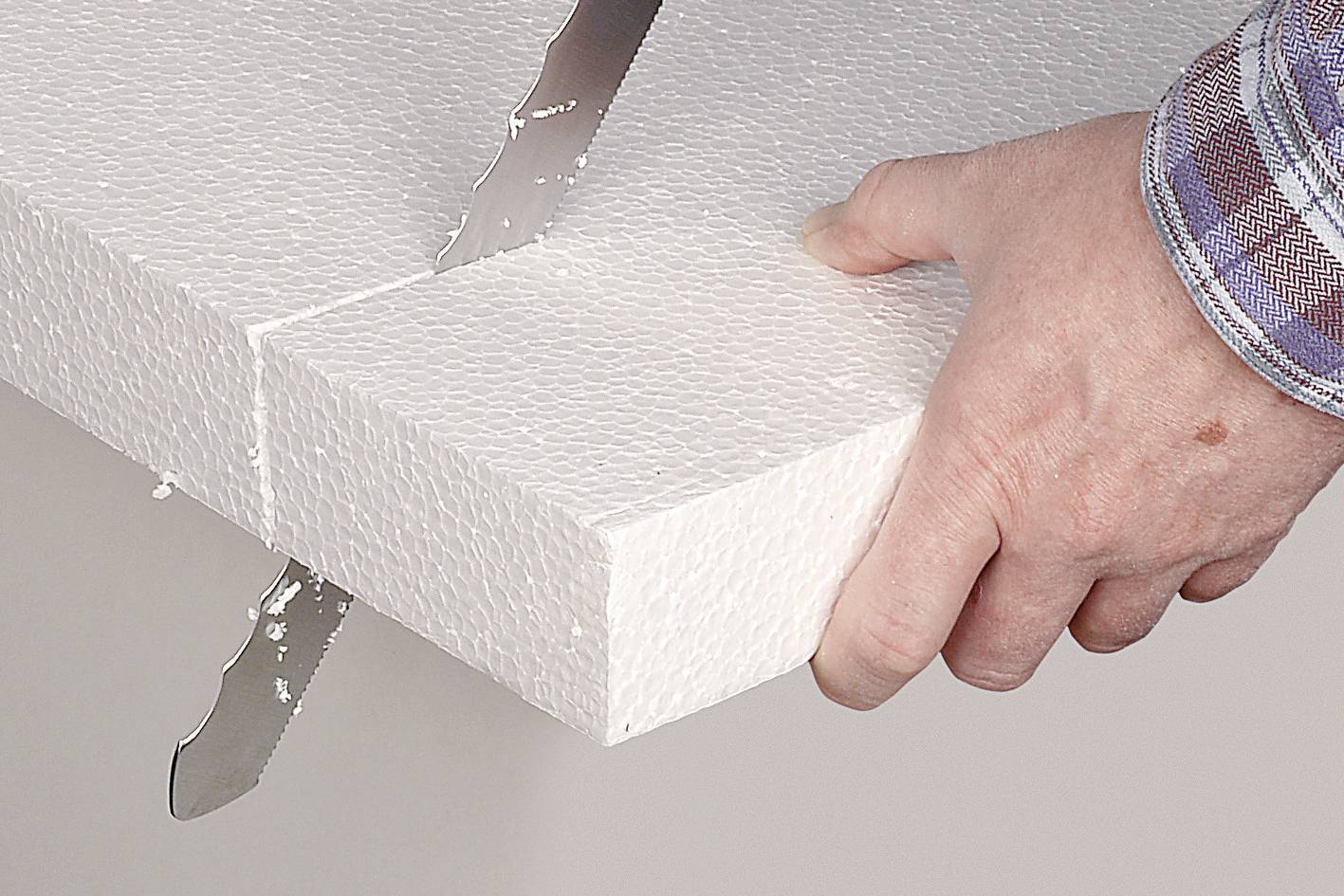 Eine Hand hält eine weiße Styroporplatte, während sie mit einem gezackten Messer geschnitten wird.