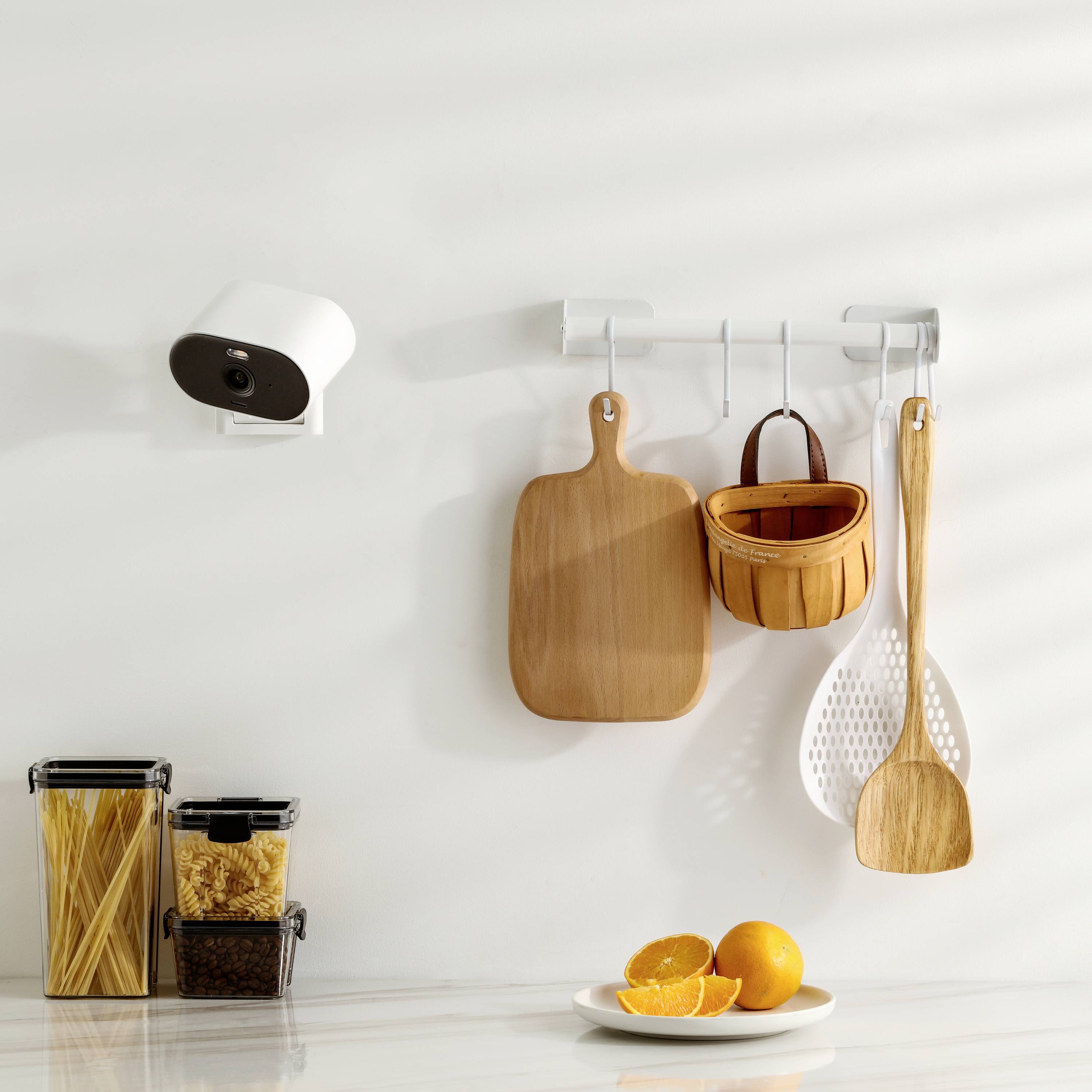 Küche mit Kamera an der Wand, Schneidebrett, Holzkelle sowie Einmachgläser mit Nudeln und Reis auf einer hellen Arbeitsfläche.