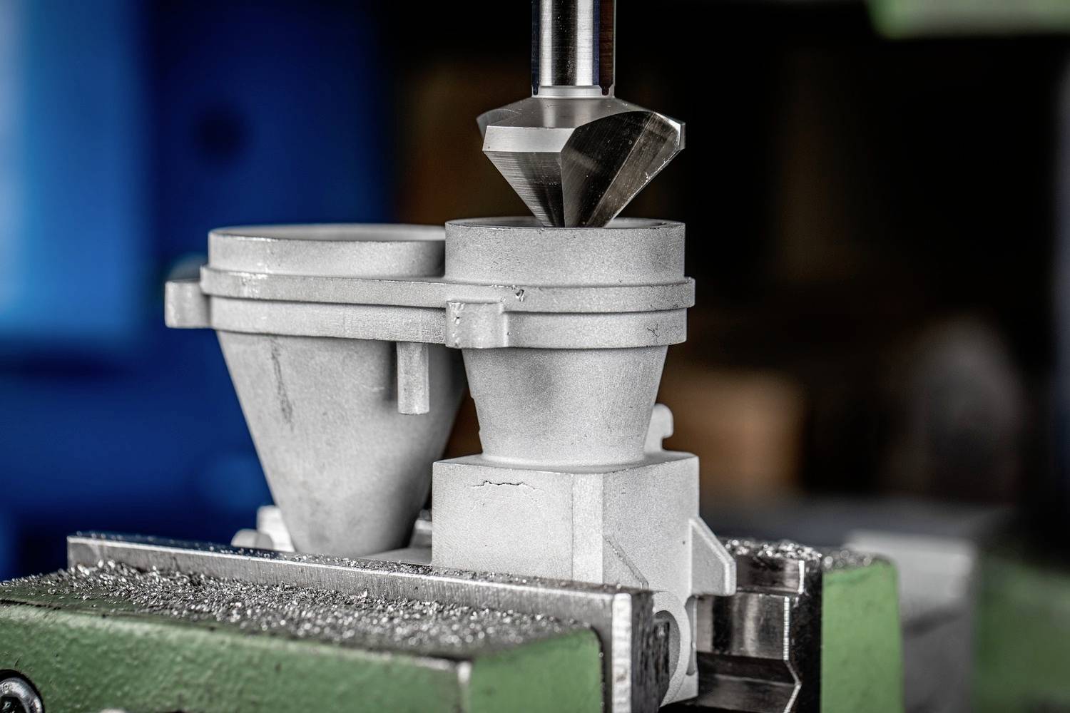 Eine Metallbohrmaschine bearbeitet präzise die Oberfläche eines Werkstücks. Im Hintergrund ist unscharfe Werkstattausrüstung zu sehen.