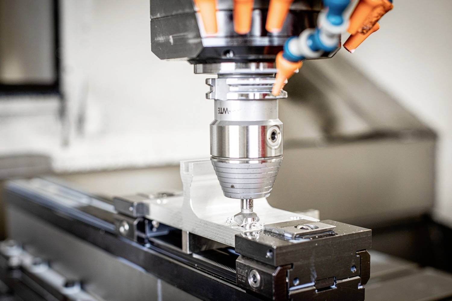 Eine CNC-Fräse bearbeitet ein Metallstück, indem sie präzise Formen und Strukturen formt. Orange Schläuche führen Kühlmittel hinzu.