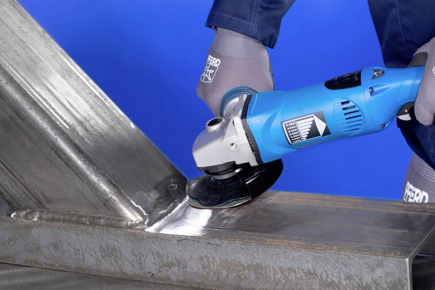 Person schleift eine Schweißnaht auf einem Metallwerkstück mit einem Winkelschleifer. Hintergrund ist einheitlich blau.