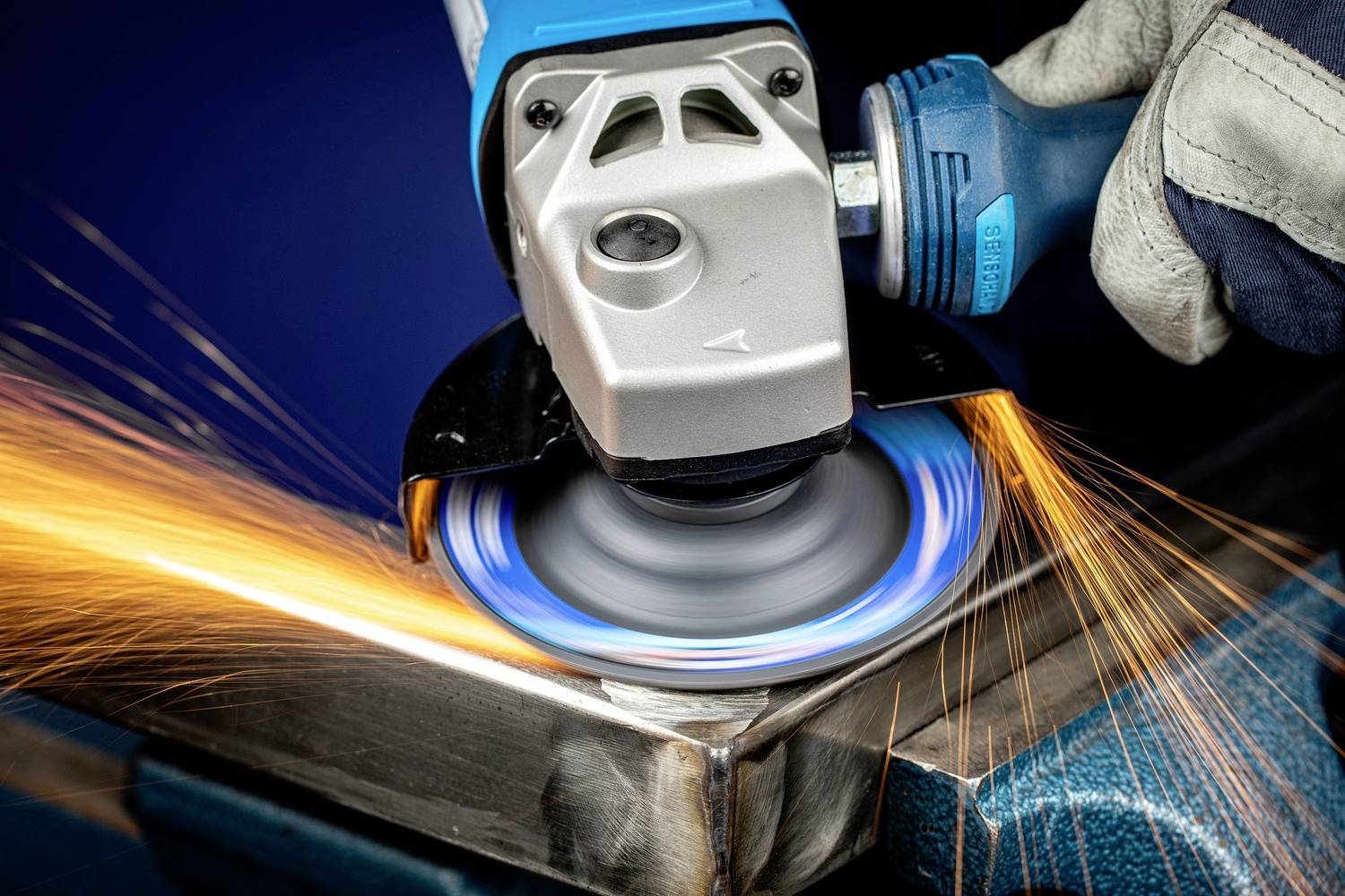 Ein Arbeiter schleift ein Metallstück mit einer Winkelschleifmaschine. Funken sprühen von der bearbeiteten Kante.