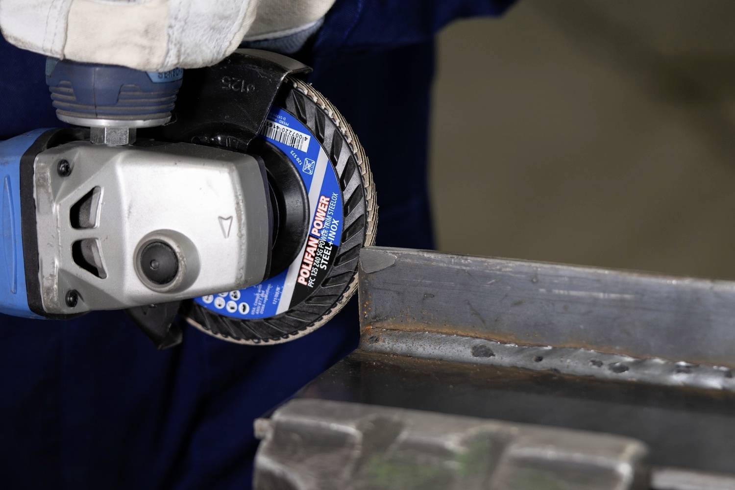 Eine Person schleift eine Metallkante mit einer elektrischen Schleifmaschine, um sie zu glätten. Fokus liegt auf der Schleifscheibe.