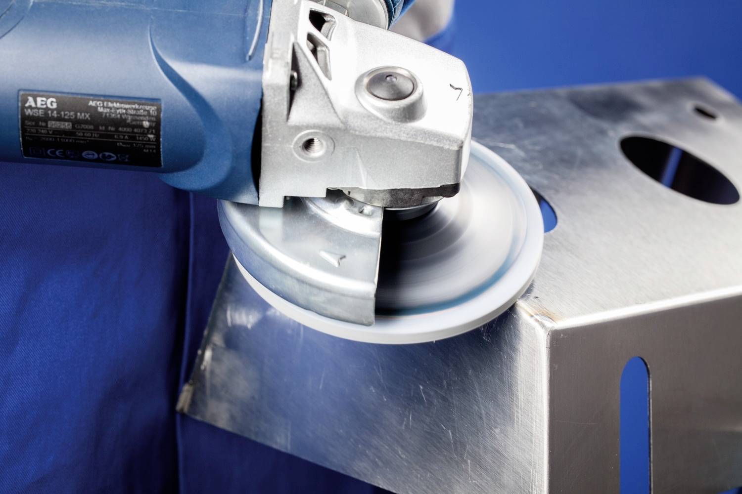 Ein Winkelschleifer in Betrieb, der einen Metallblock glättet. Bewegungsunschärfe zeigt die Rotation der Schleifscheibe an.