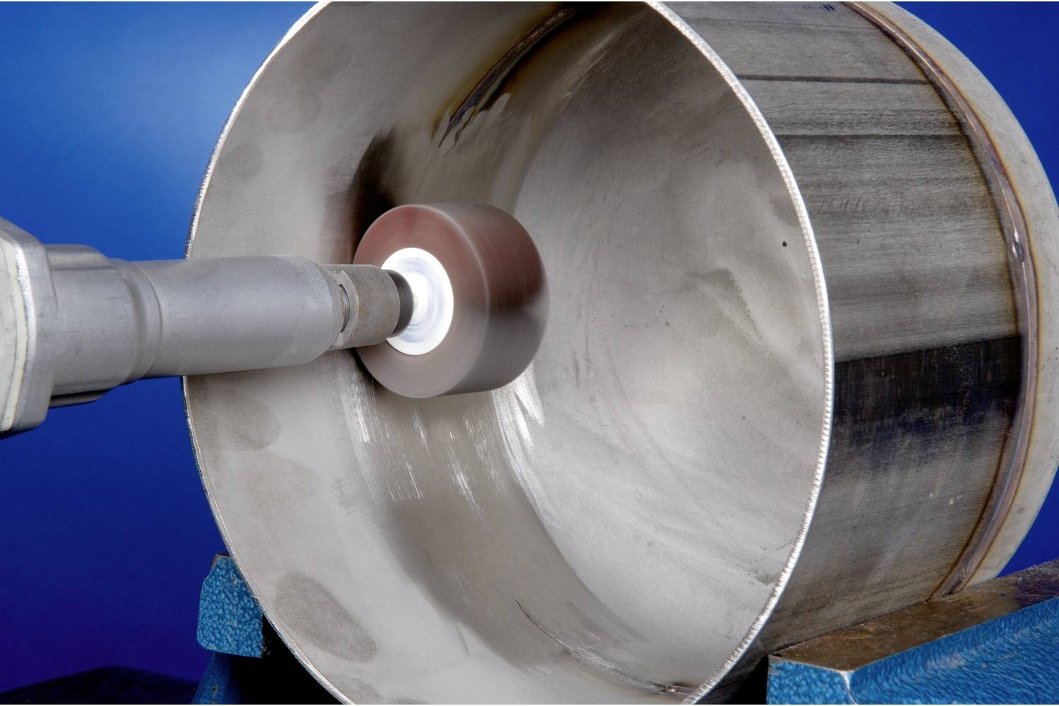 Eine Maschine im Einsatz, die die Innenseite eines Metallrohrs poliert. Das Rohr ist auf einer blauen Halterung fixiert.