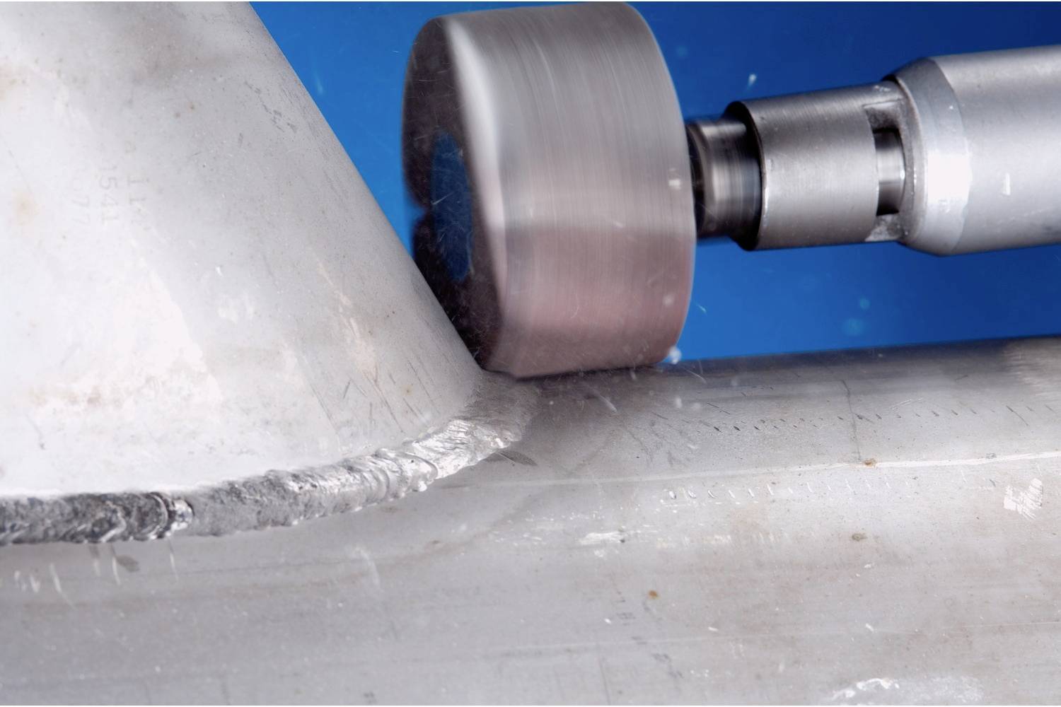 Ein Schweißroboter bearbeitet präzise eine Metallnaht an einem Rohr auf blauem Grund, zeigt industrielle Automatisierung im Einsatz.