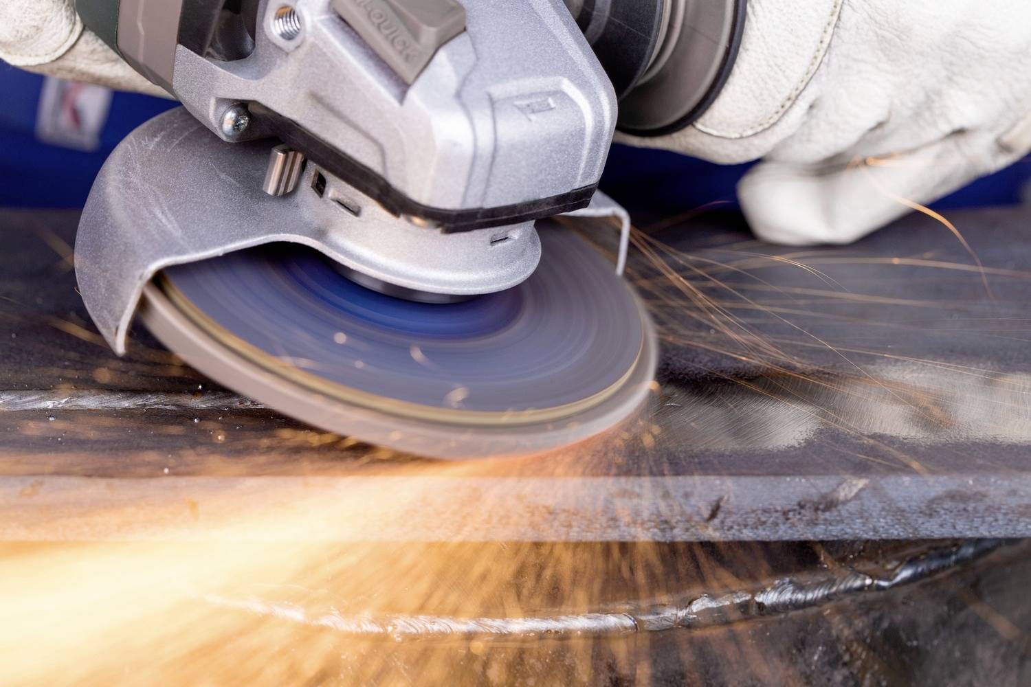 Eine Hand hält einen Winkelschleifer, der Funken sprüht, während er Metall schleift. Schutzkleidung ist sichtbar.