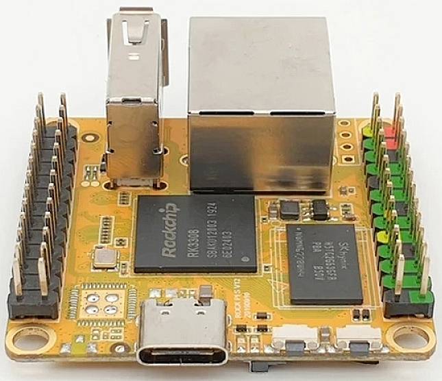 Ein kleines, orangefarbenes Computer-Board mit Chips, USB-C-Anschluss und mehreren Pins für elektronische Verbindungen.