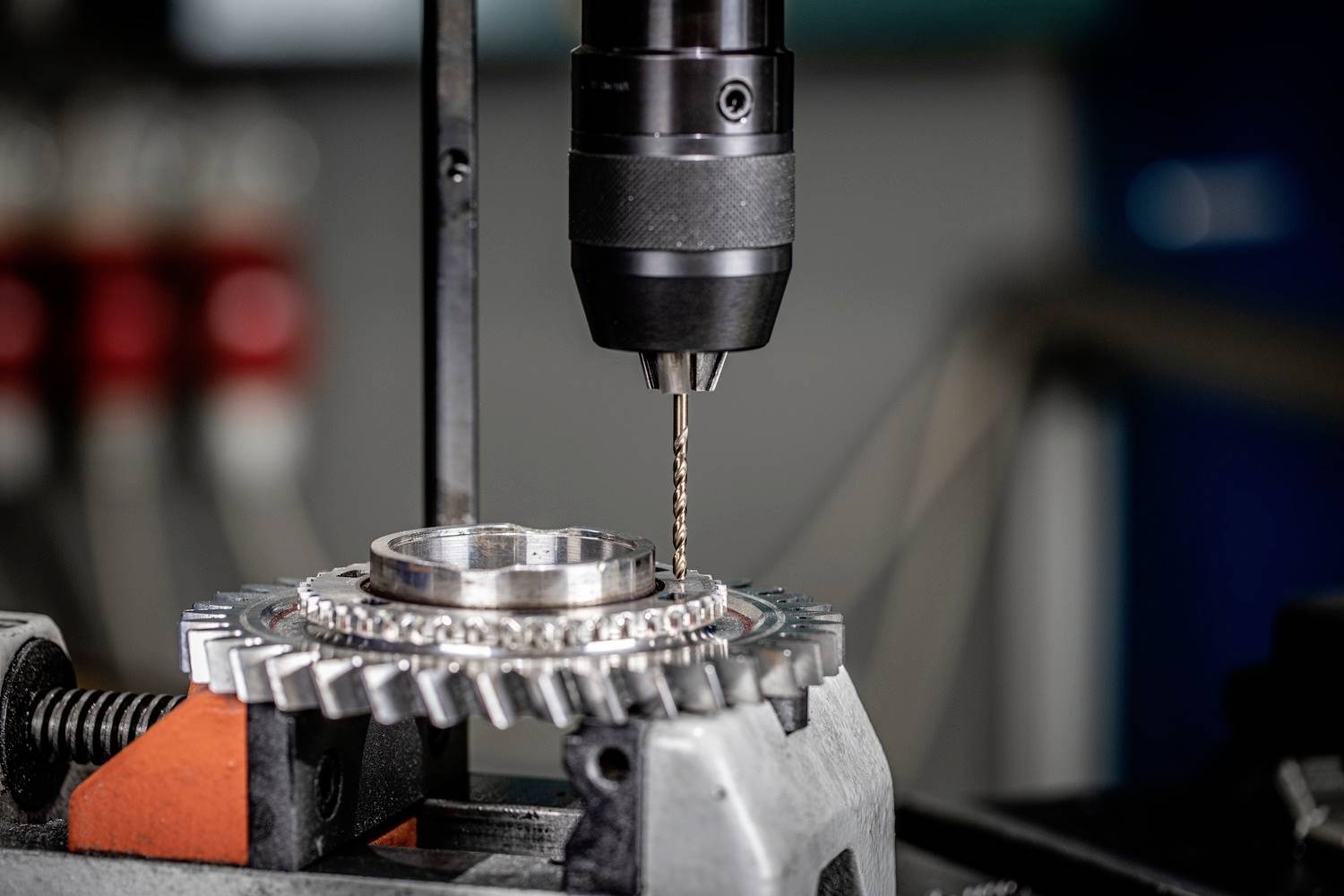 Eine Bohrmaschine bearbeitet ein Zahnrad in einer Werkstatt. Der Bohrer ist präzise auf dem Metall positioniert. Mechanisches Detail sichtbar.