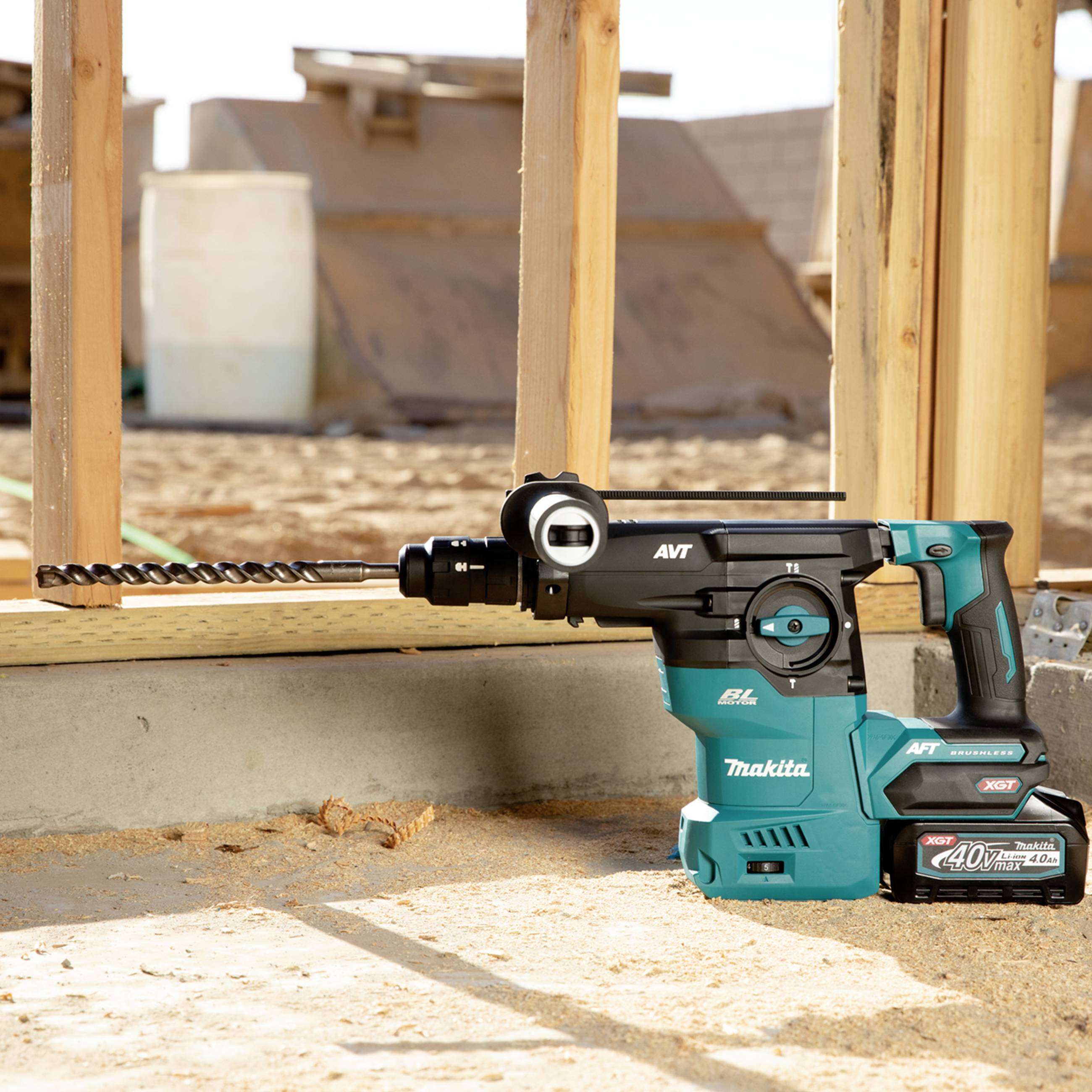 Ein elektrischer Bohrhammer bohrt ein Loch in einen Holzrahmen auf einer Baustelle, mit einer Batterie von Makita im Hintergrund.