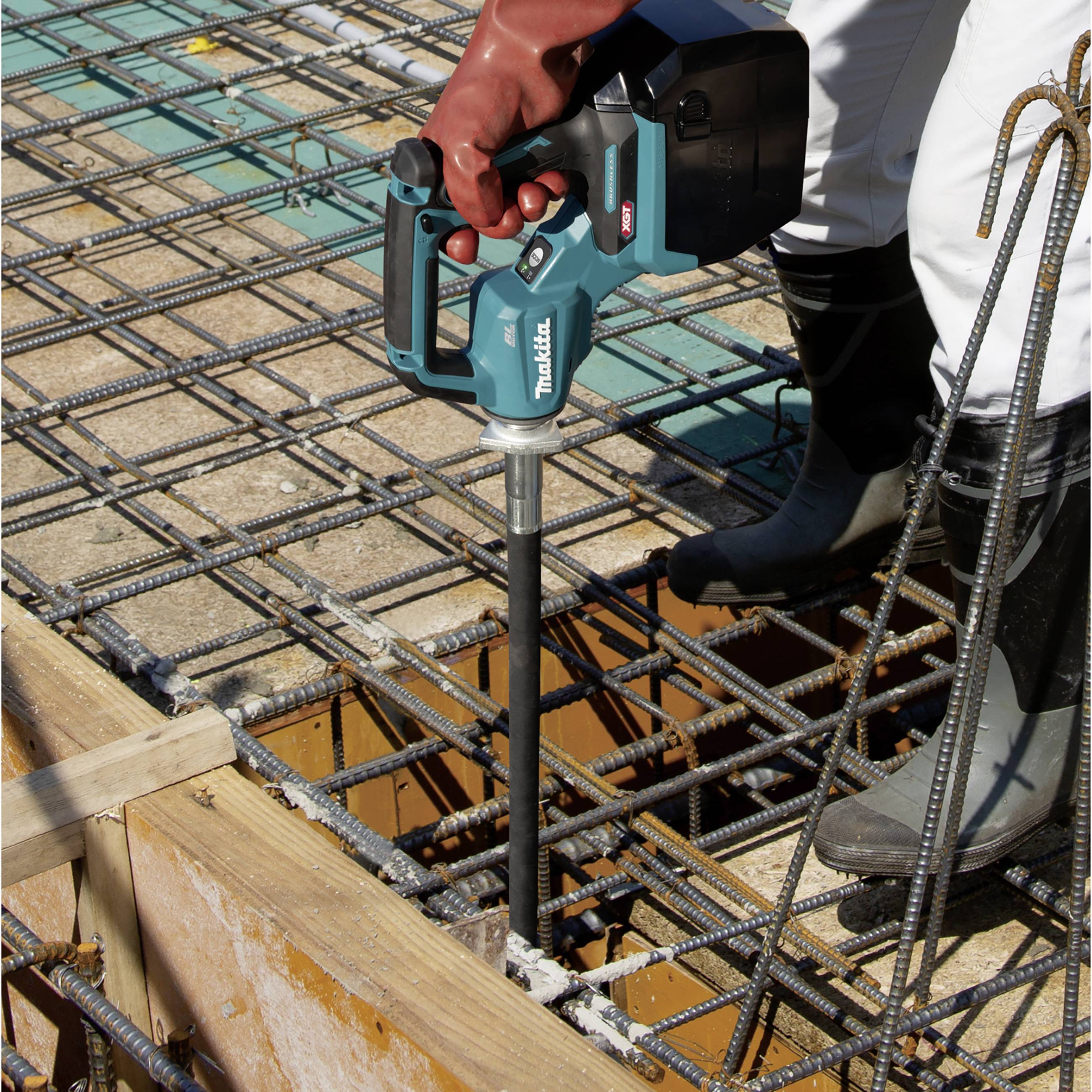 Ein Arbeiter verwendet ein elektrisches Werkzeug zur Betonverdichtung auf einer Baustelle mit Stahlbewehrung.