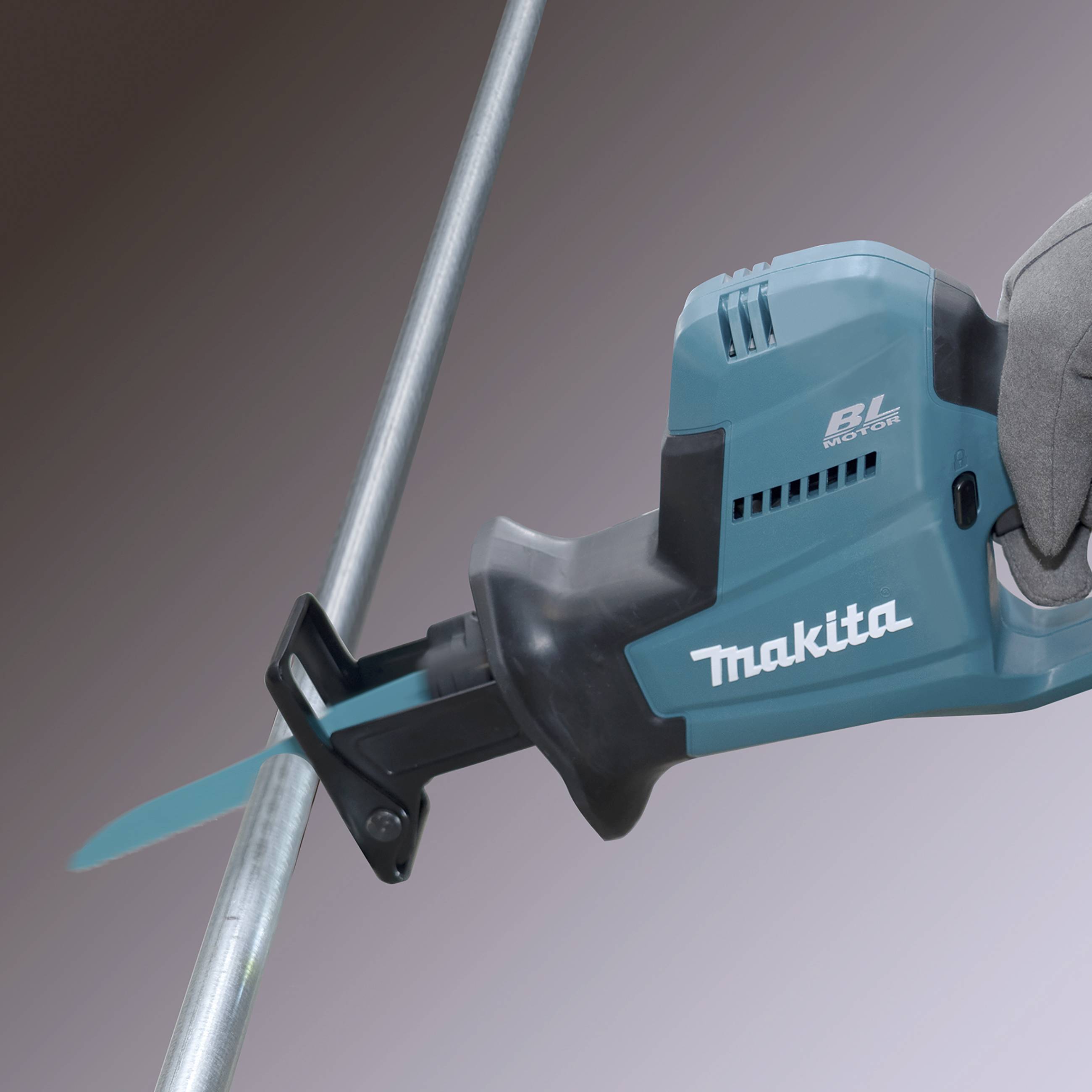 Eine Akku-Säbelsäge schneidet ein Metallrohr. Die Säbelsäge ist blau und schwarz, mit der Aufschrift 'Makita BL Motor'.