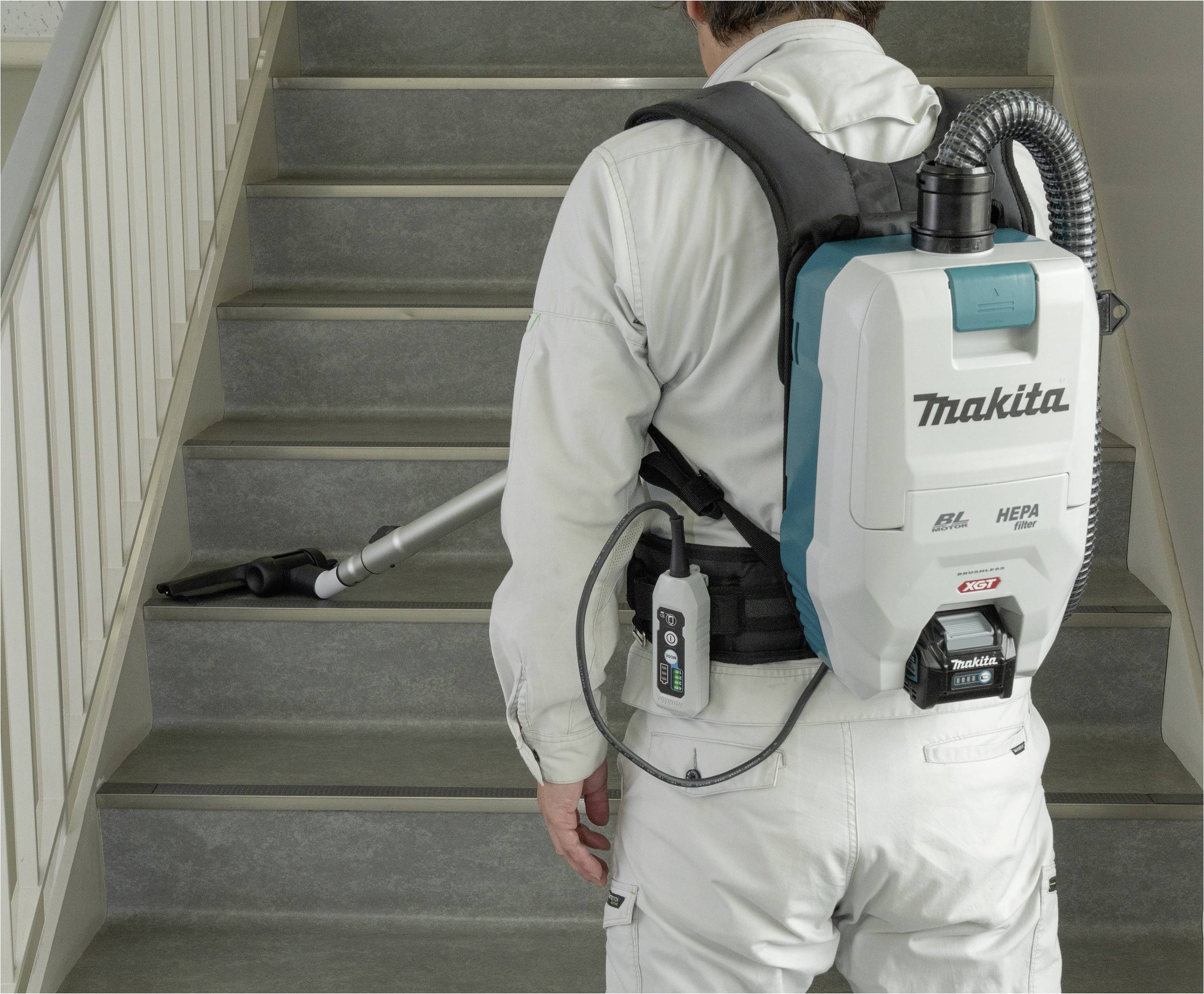 Eine Person in Arbeitskleidung benutzt einen rückentragbaren Staubsauger, um eine Treppe zu reinigen. Der Staubsauger hat einen HEPA-Filter.