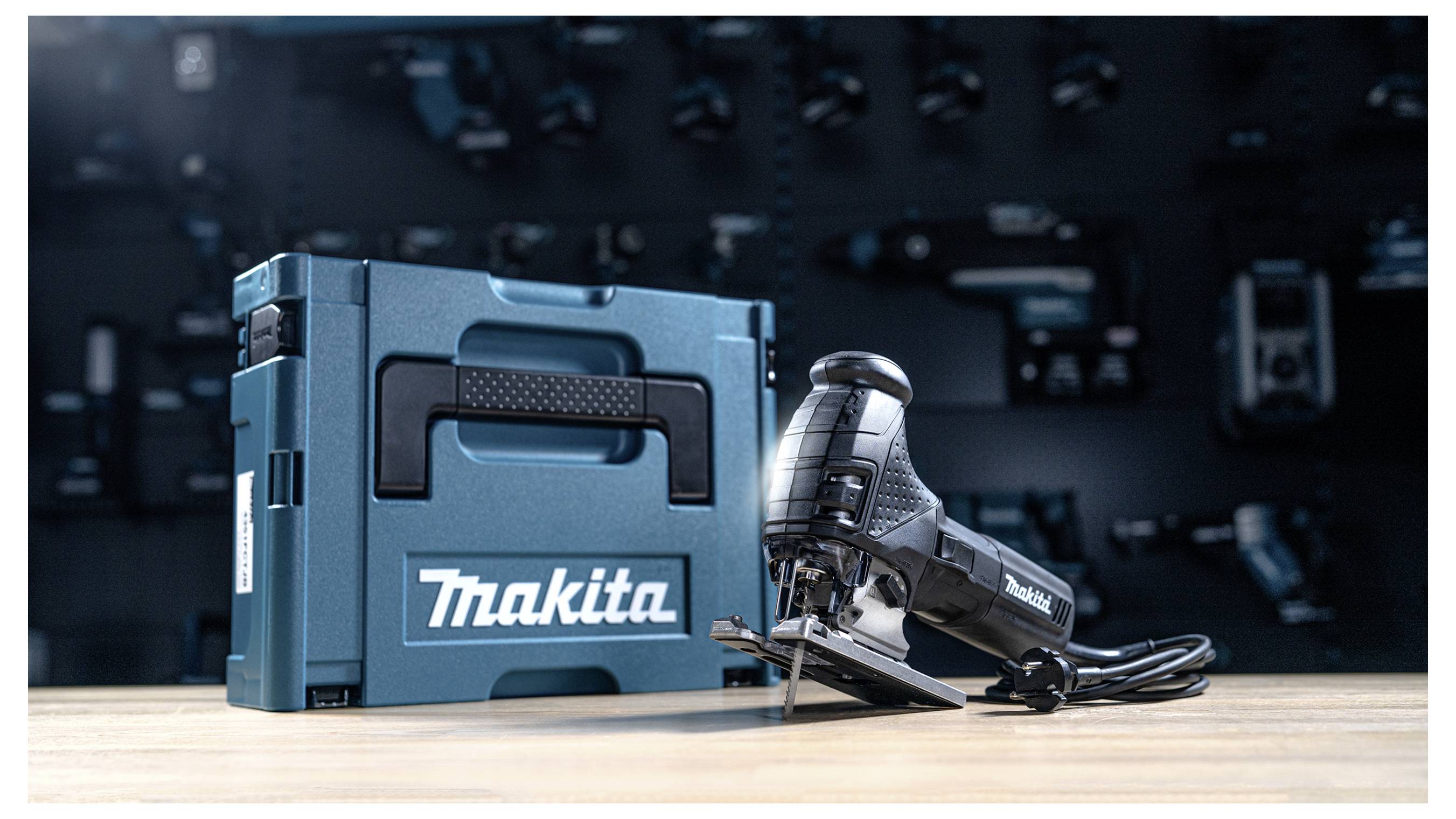 Eine Makita Stichsäge mit Transportkoffer auf einer Werkbank, mit einem unscharfen Hintergrund von Werkzeugen, was eine Werkstattumgebung andeutet.