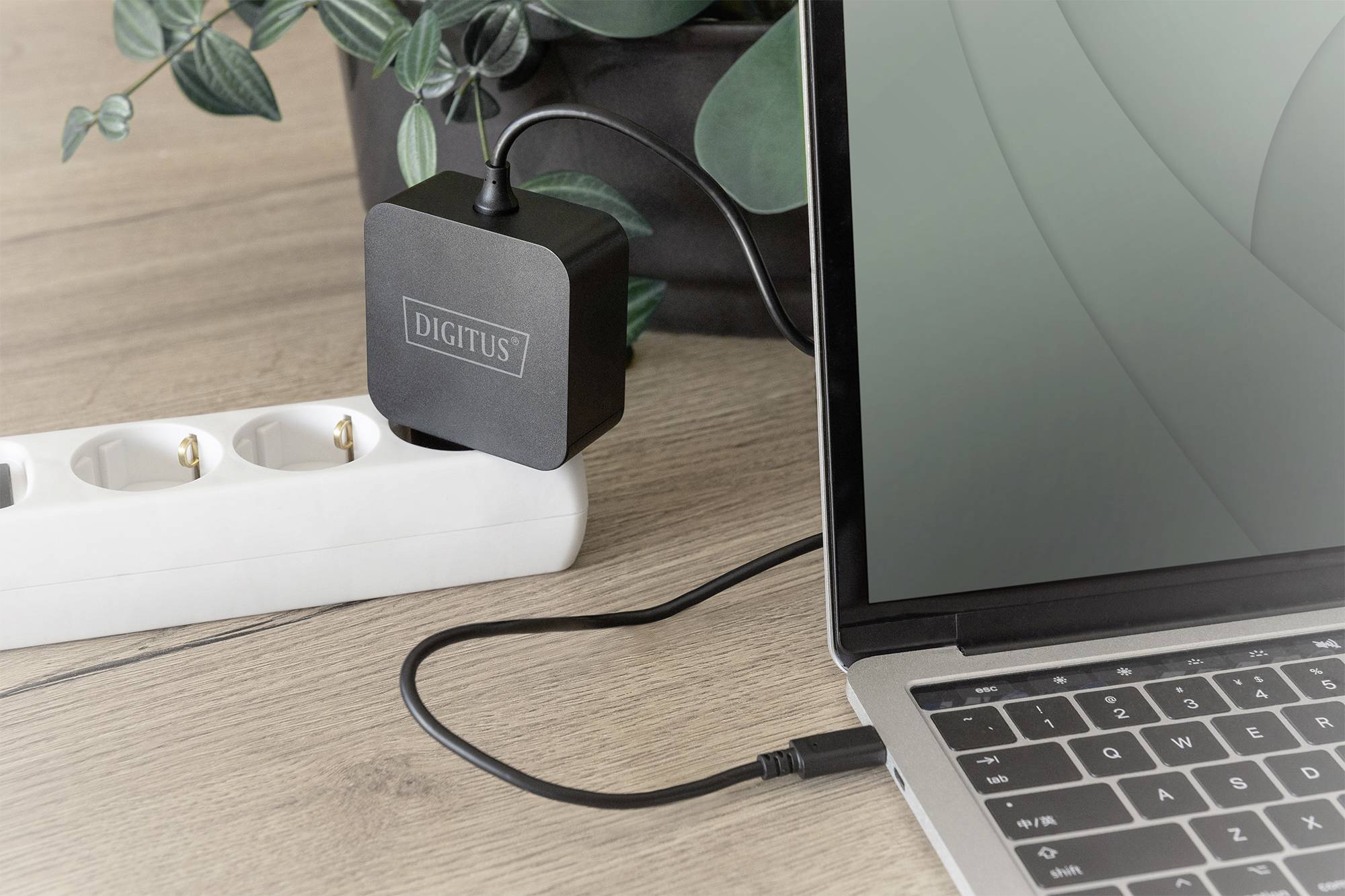 Das Bild zeigt einen Laptop, der mit einem Netzgerät verbunden ist. Das Netzgerät steckt in einer Steckdosenleiste.
