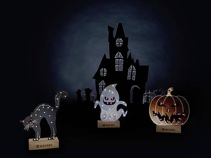 Drei Halloween-Dekorationen vor einem dunklen, gespenstischen Haus: eine schwarze Katze, ein lachender Geist und ein geschnitzter Kürbis mit Fledermäusen.