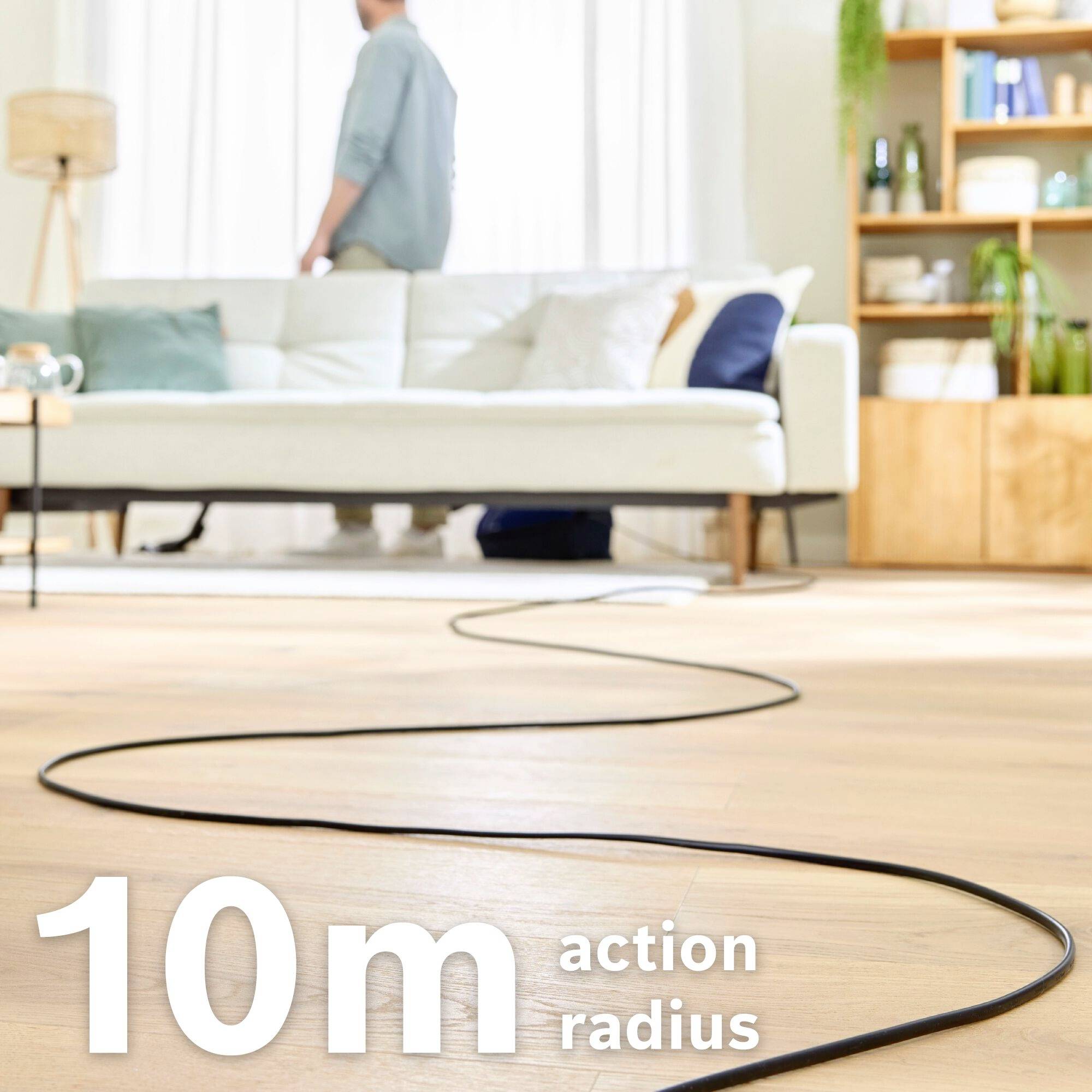 '10 m Aktionsradius' auf Holzboden, im Hintergrund Sofa und Mann mit hellem Hemd stehend.