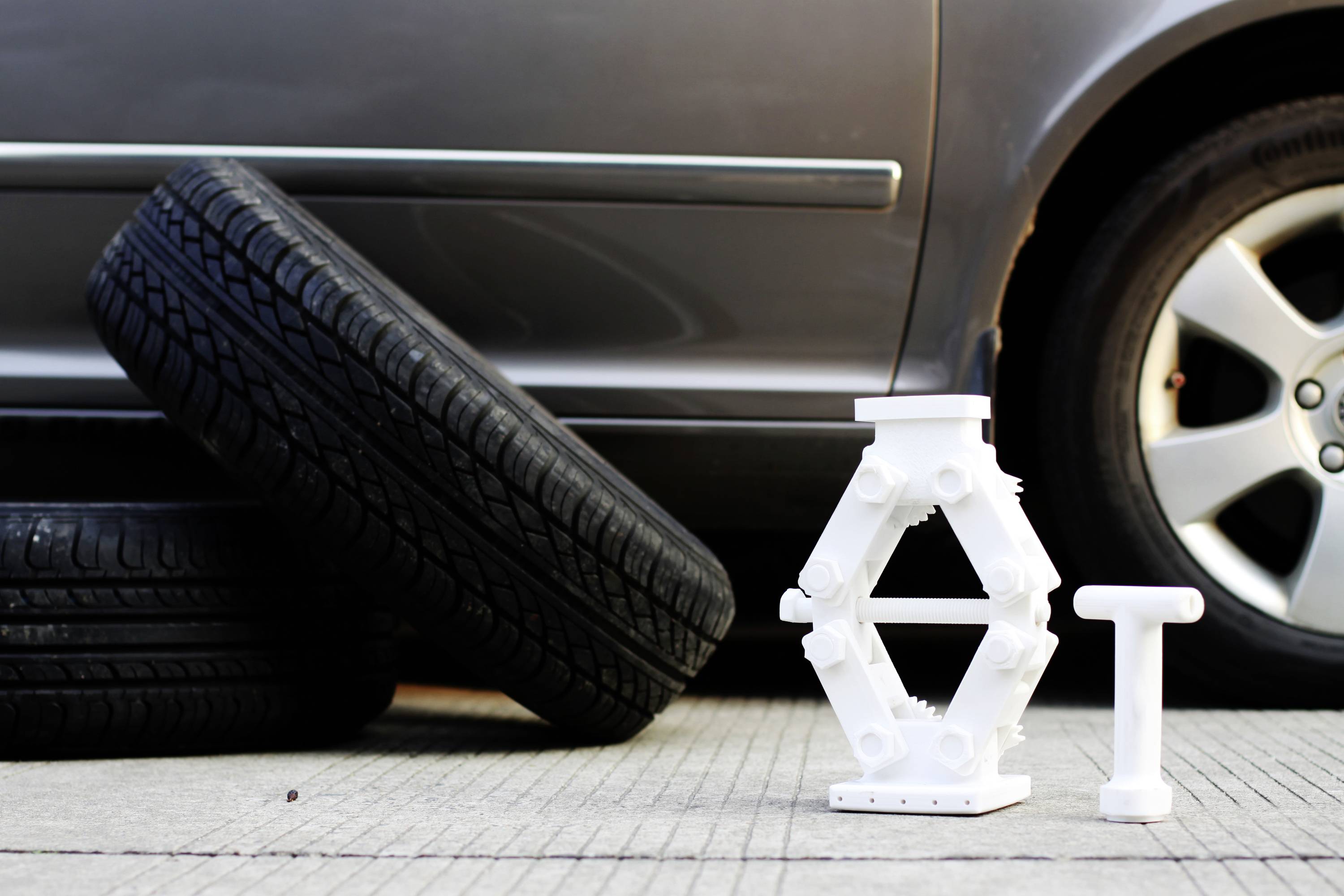 Ein Autoheber und ein Radkreuzschlüssel vor einem Auto mit zwei abmontierten Reifen, das auf einem Bürgersteig geparkt ist.