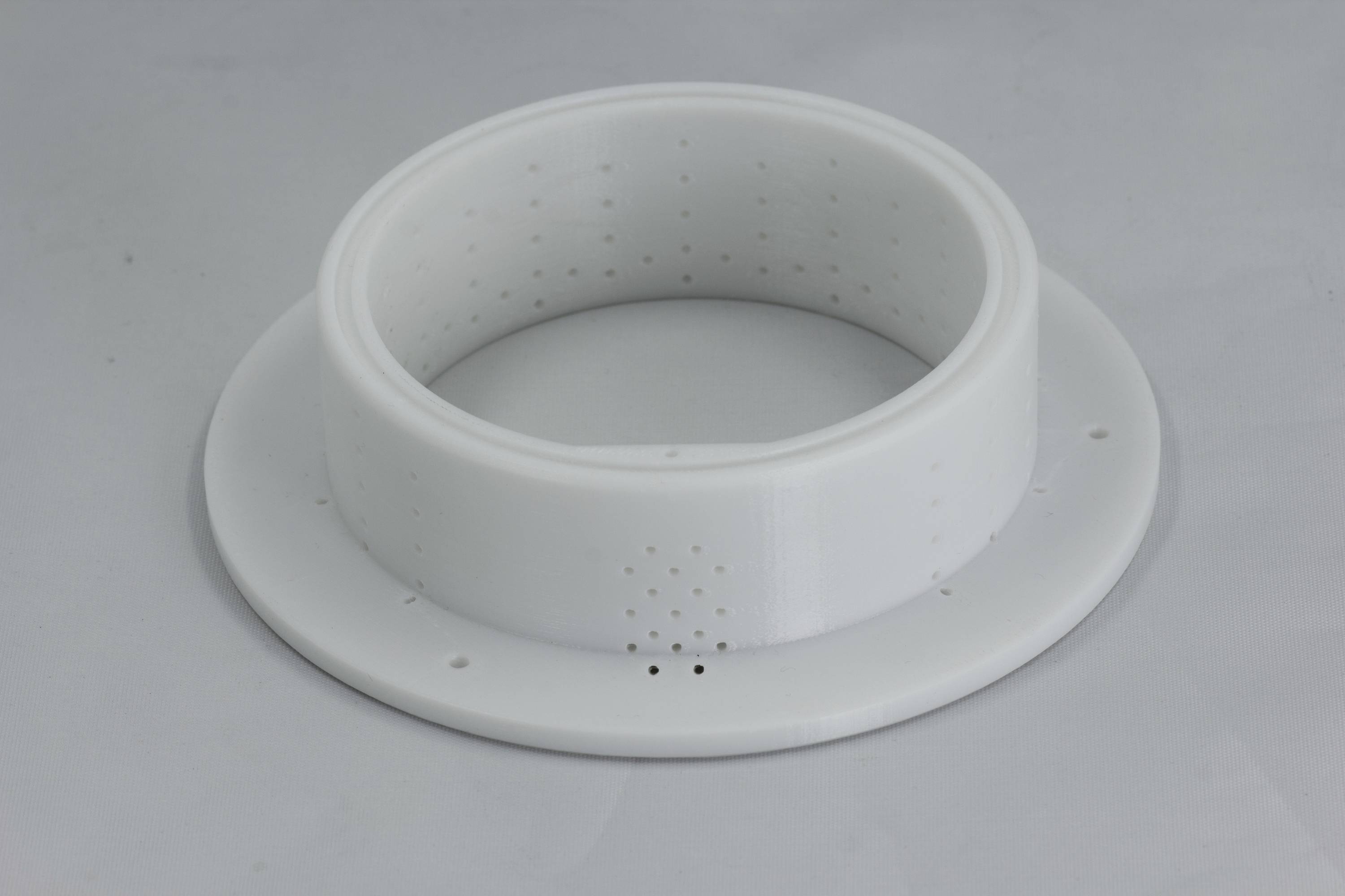 Ein weißer Plastikring mit Löchern auf einem grauen Hintergrund. Der Ring hat eine zylindrische Form und eine flache Basis.