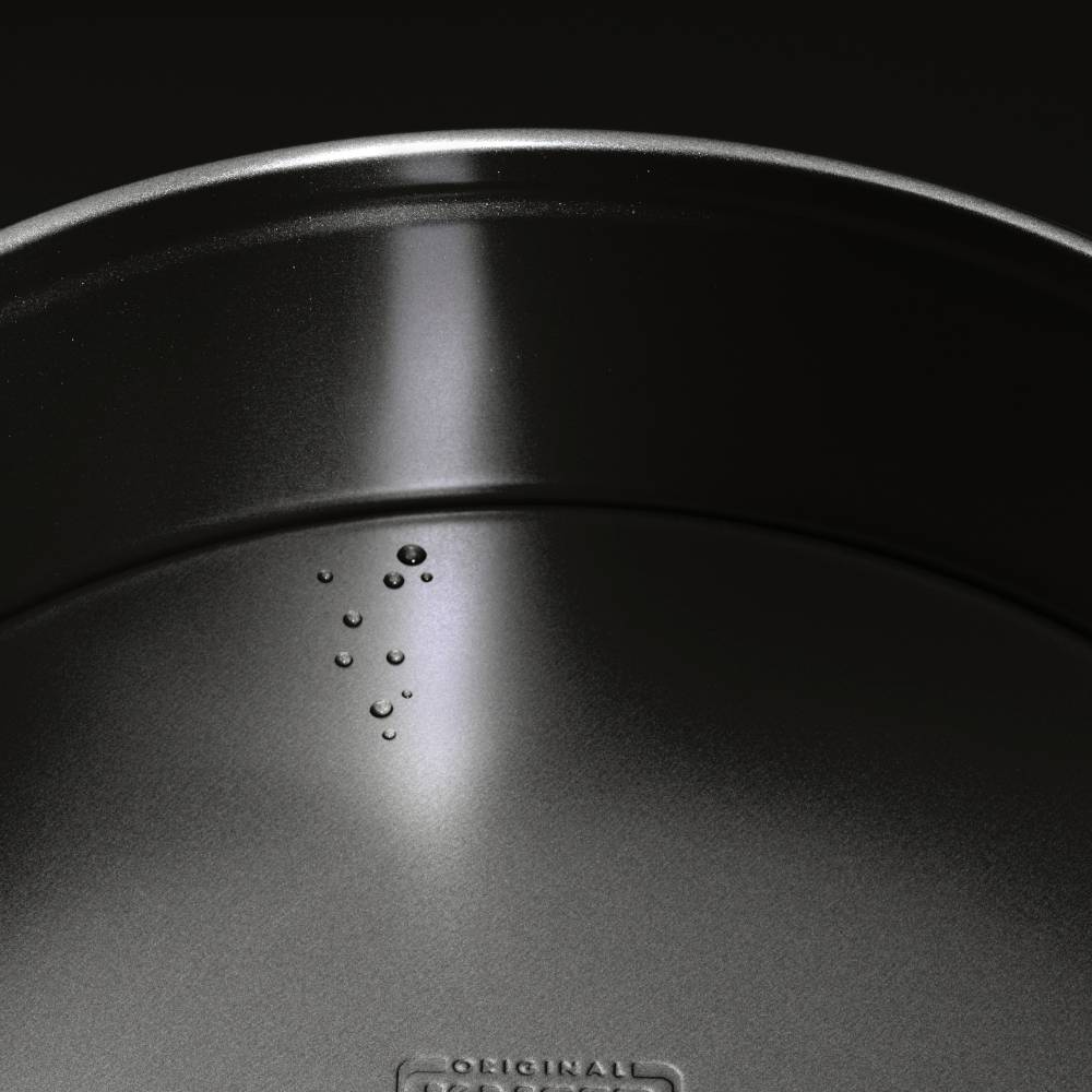 Eine schwarze metallische Oberfläche mit Wassertropfen, die auf einer Seite verteilt sind. Leicht glänzende Struktur im Licht.