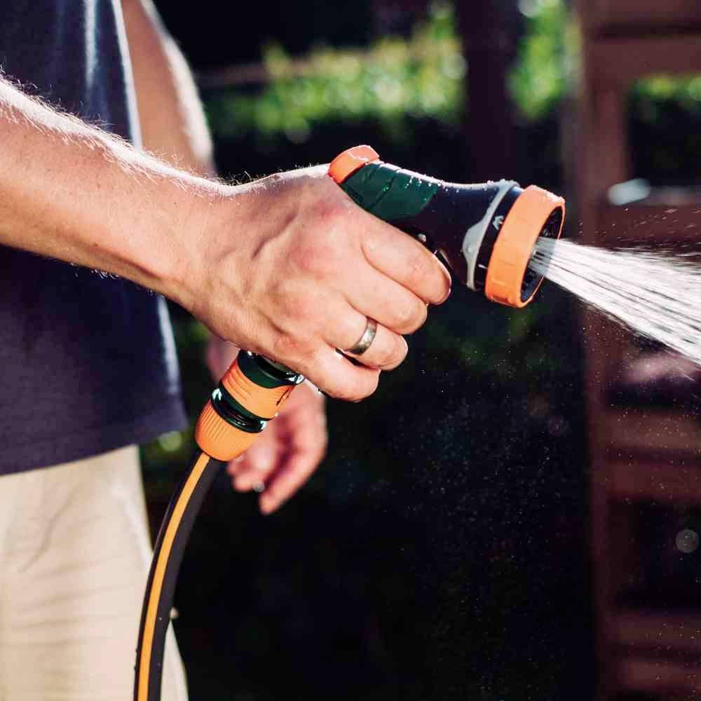 Eine Person hält einen Gartenschlauch mit einer Sprühdüse und bewässert den Garten.