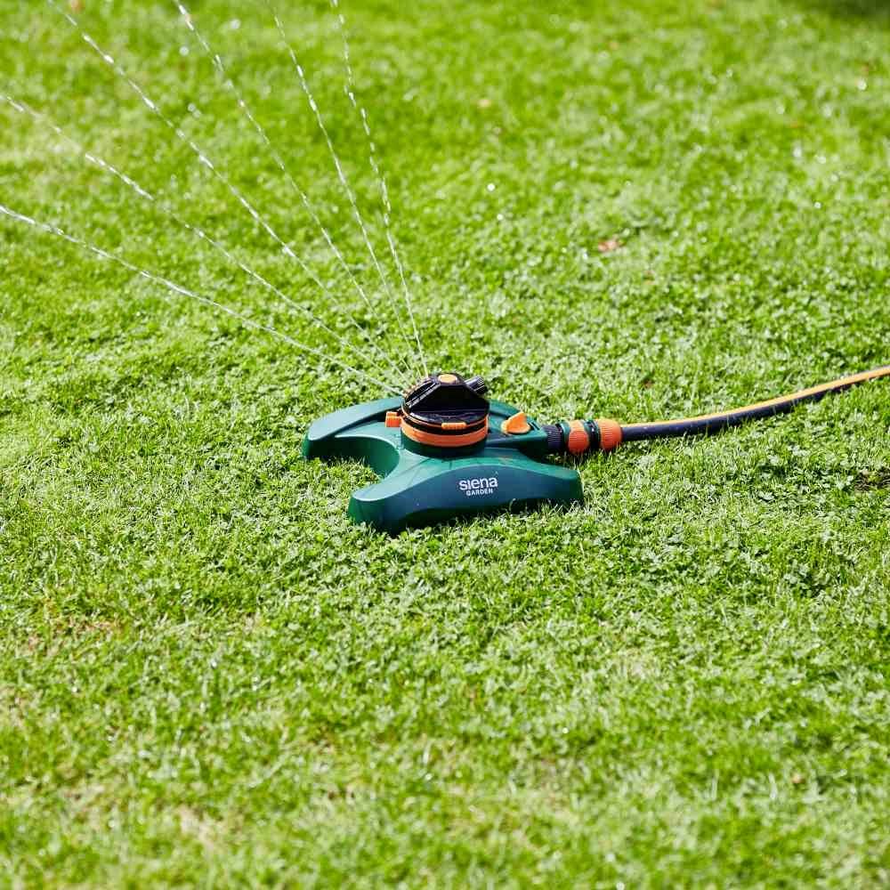 Ein automatischer Rasensprinkler auf grünem Gras sprüht Wasser in mehrere Richtungen.