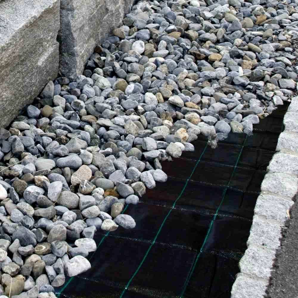 Eine Drainagegrube mit Kies gefüllt, umgeben von Steinplatten zur Stabilisierung. Sie dient zur Entwässerung von Regenwasser.