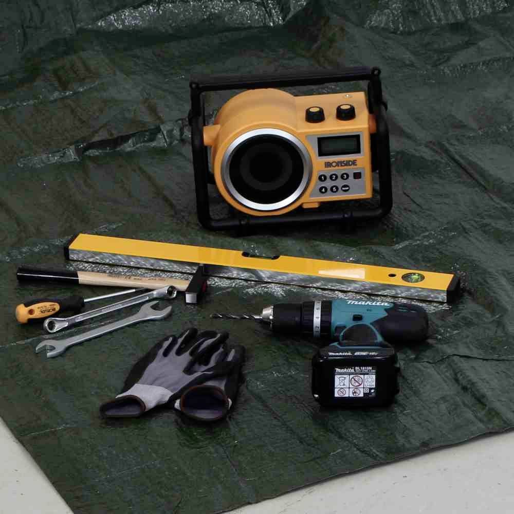 Werkzeuge auf einer Plane: Wasserwaage, Handschuhe, Schraubenschlüssel, Schraubenzieher, Bohrmaschine, Kamera.