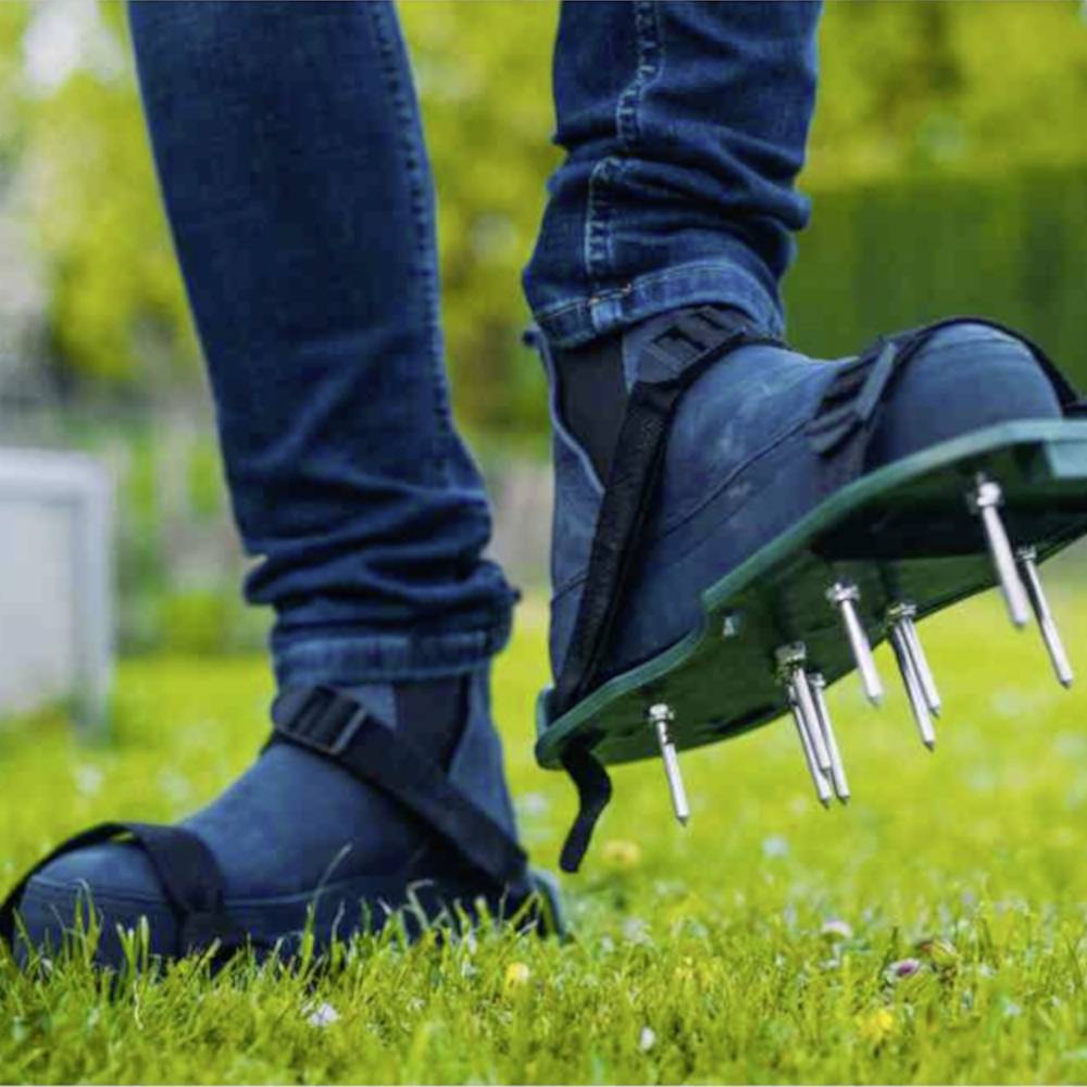 Person trägt Spikes-Sandalen auf einer grünen Wiese, wahrscheinlich um den Rasen zu lüften. Nahaufnahme von Beinen und Schuhen.