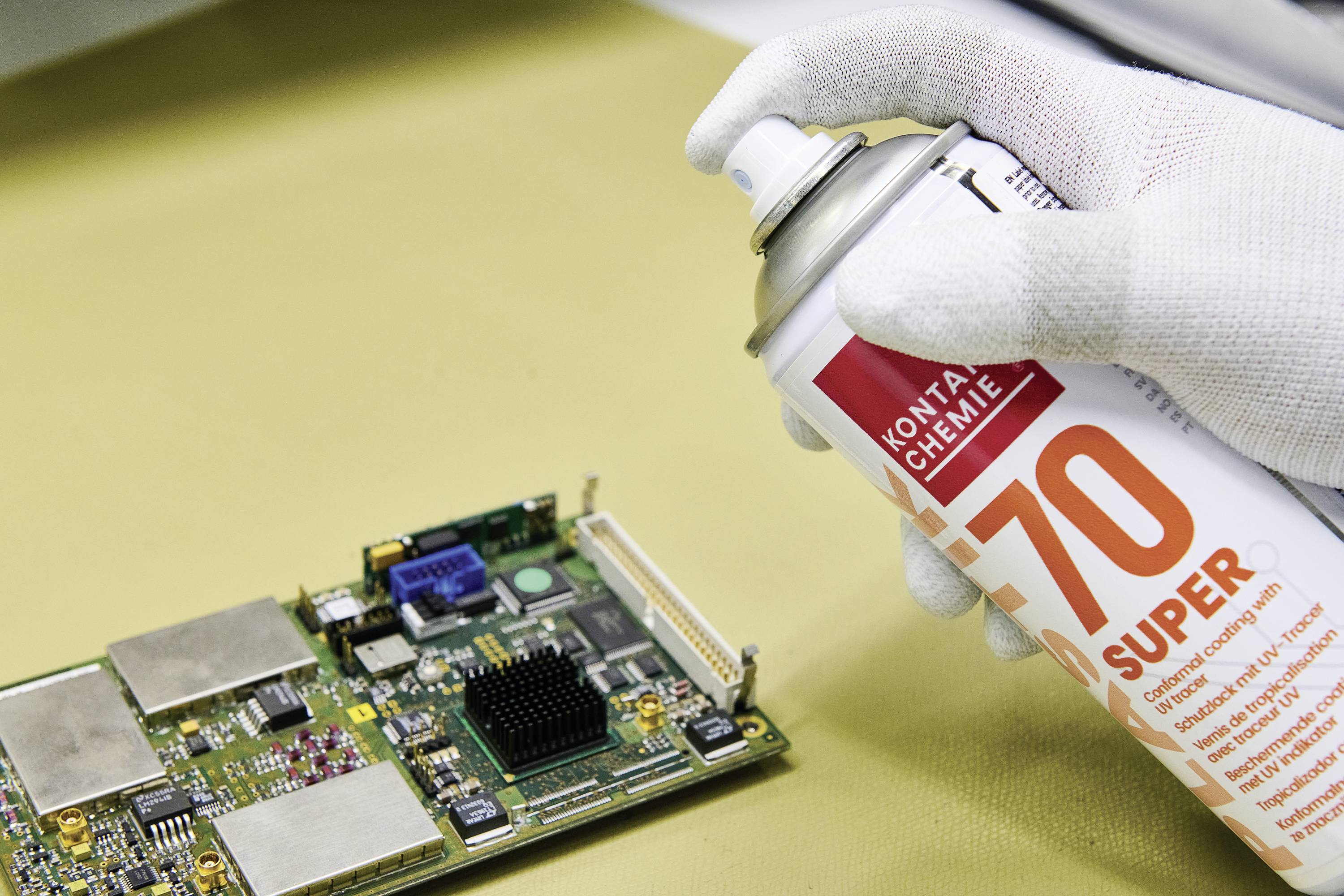 Eine Hand, die einen Spraydosenreiniger auf eine Computerplatine sprüht, zeigt einen Reinigungsvorgang für elektronische Komponenten.