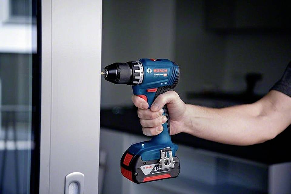 Eine Hand hält einen blauen Akkubohrschrauber vor einem Fenster.