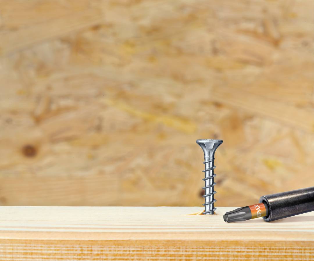Eine Schraube und ein Schraubendreher liegen auf einem Holztisch vor einem unscharfen Holz-Hintergrund.