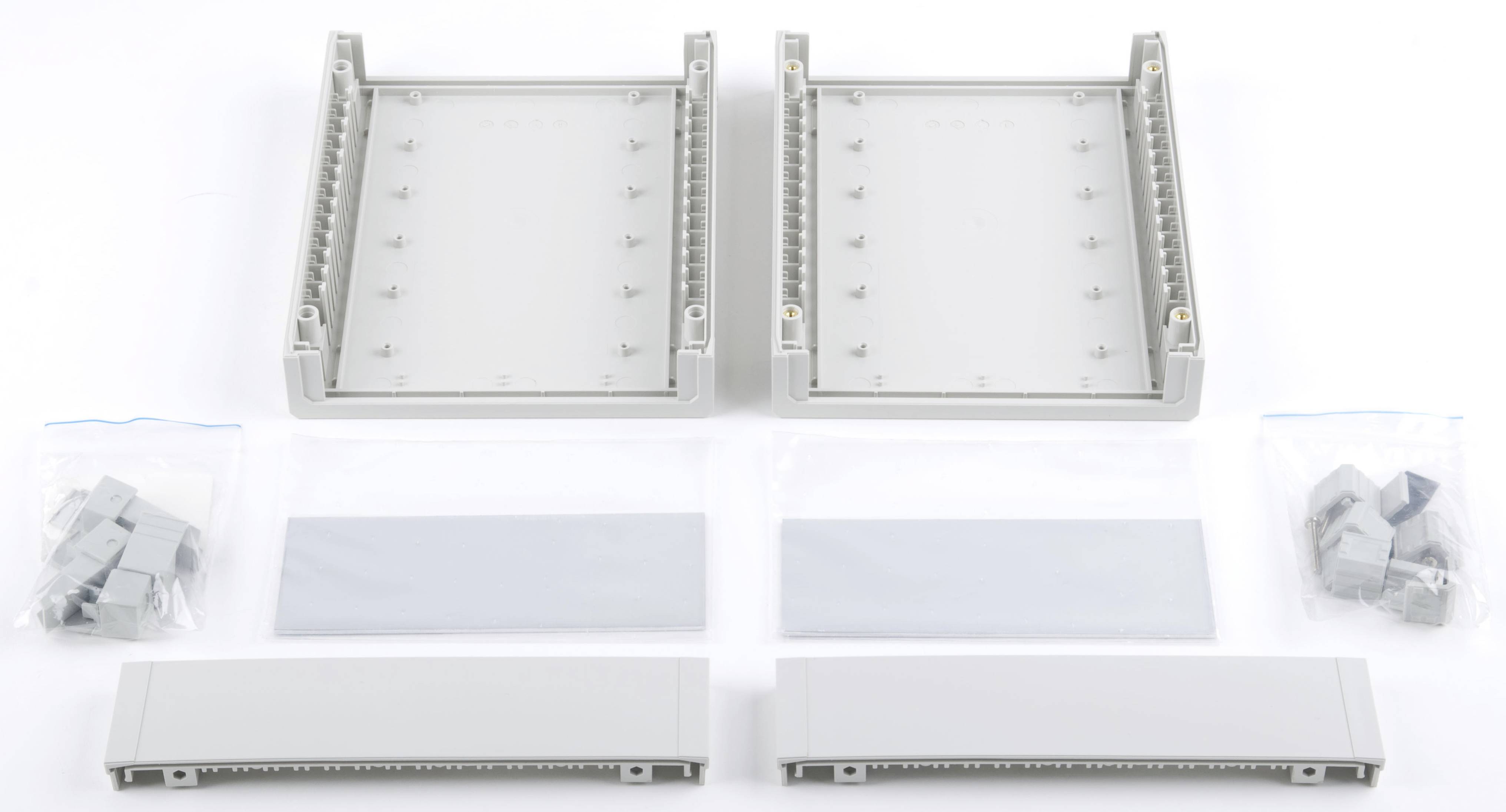 Zwei graue rechteckige Kunststoffgehäuse mit abnehmbaren Abdeckungen und zusätzlichen Befestigungselementen, auf weißem Hintergrund.