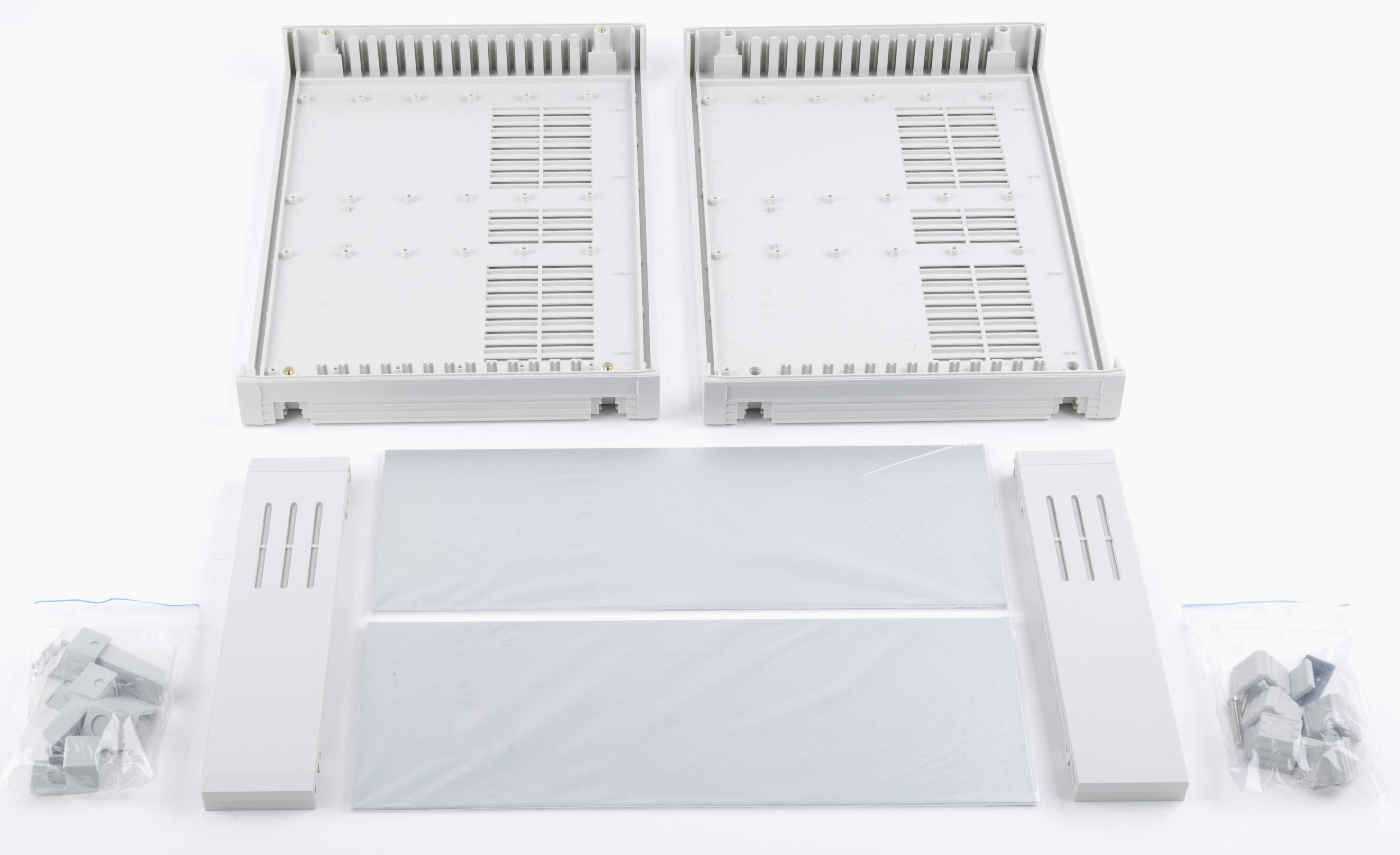 Zwei weiße Gehäuseteile, zwei Schutzblenden und drei Beutel mit Befestigungsteilen