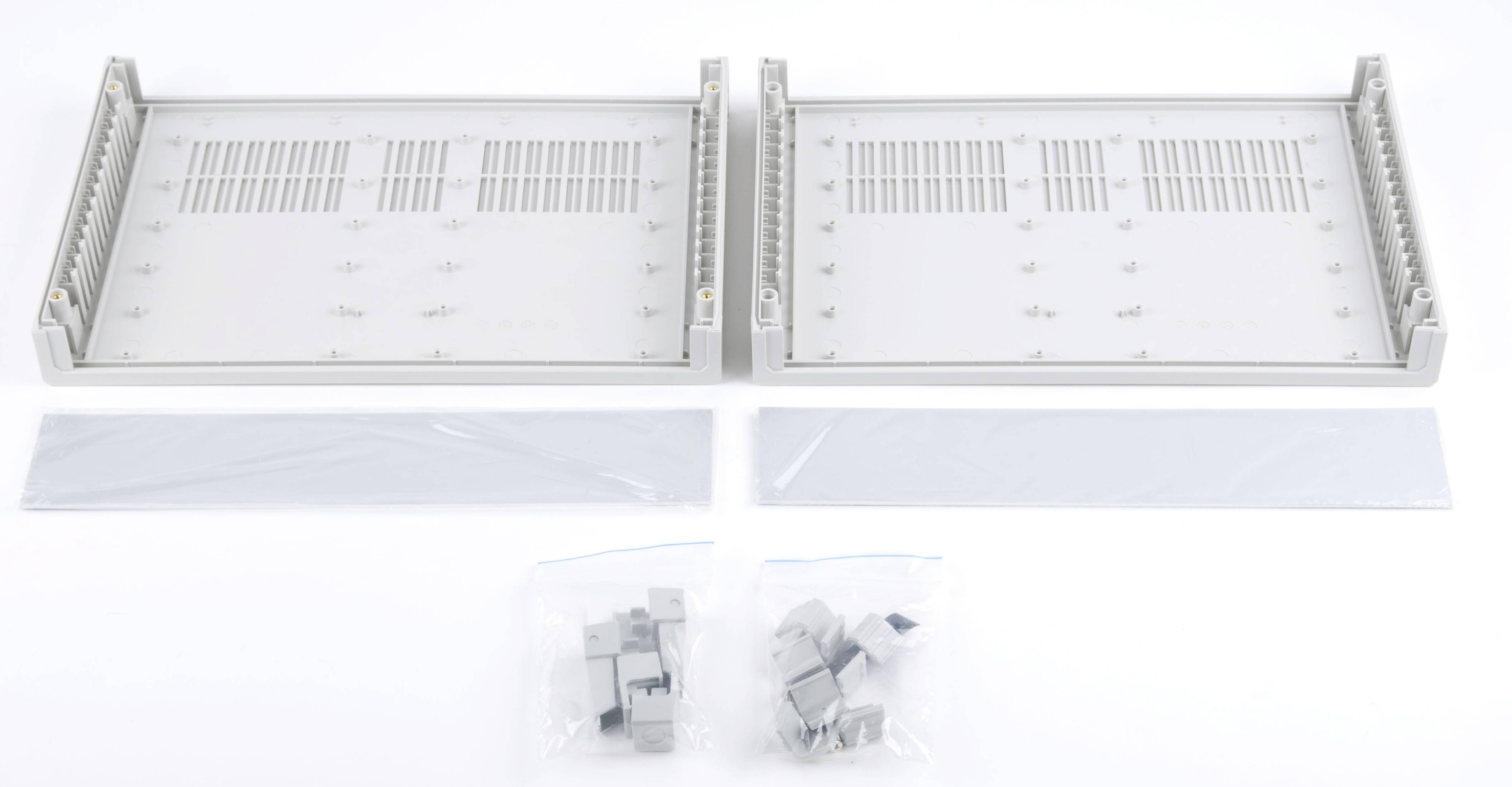 Zwei graue Metallrahmen mit Montageschienen, zwei lange Abdeckleisten und zwei Beutel mit kleinen grauen Kunststoffteilen.