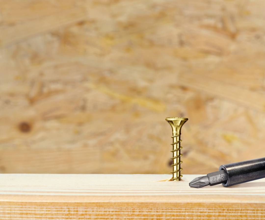 Holzschraube teilweise in Holzbrett geschraubt, daneben ein Schraubendreher. Hintergrund aus Holz. Symbolisiert handwerkliche Arbeit.