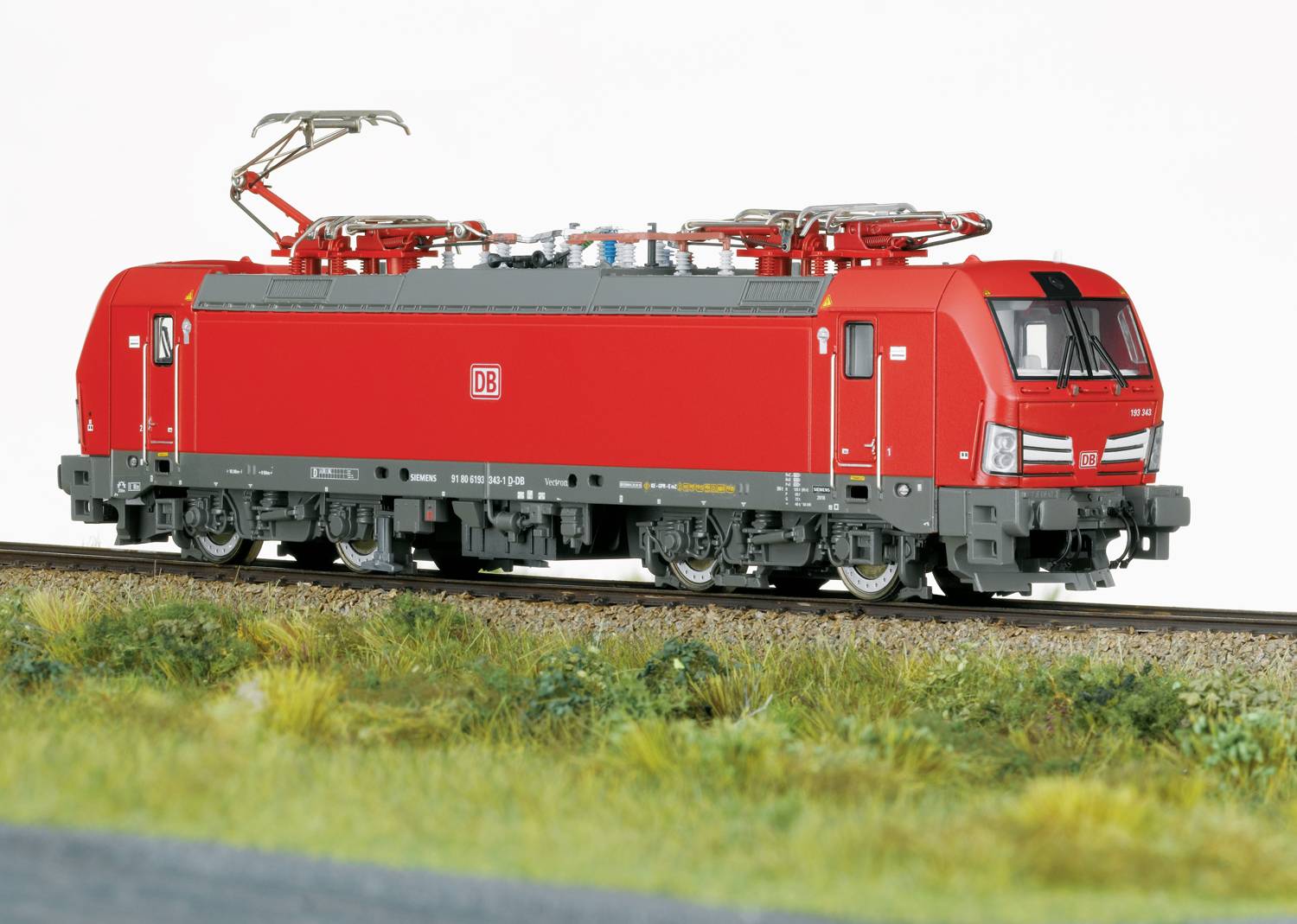 Ein rotes Modell einer Elektrolokomotive der Deutschen Bahn auf einem Gleis, umgeben von Gras.