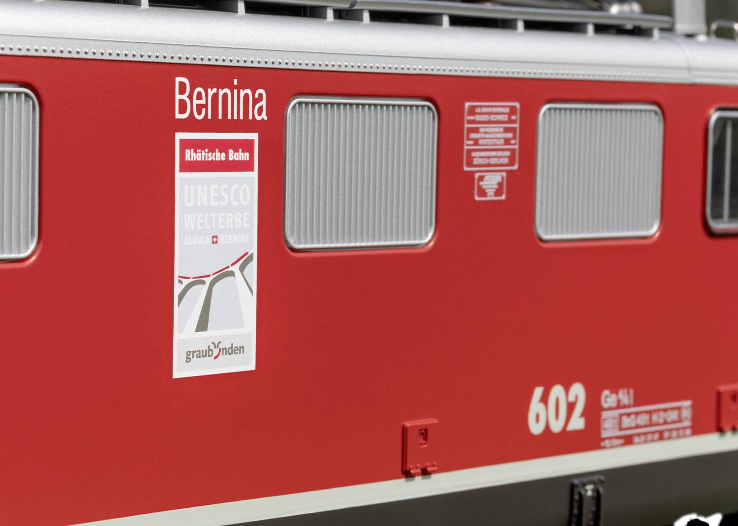 Rote Bahn mit der Aufschrift 'Bernina'. Plakat zeigt 'UNESCO Welterbe'. Modell der Rhätischen Bahn, Nummer 602, aus Graubünden.