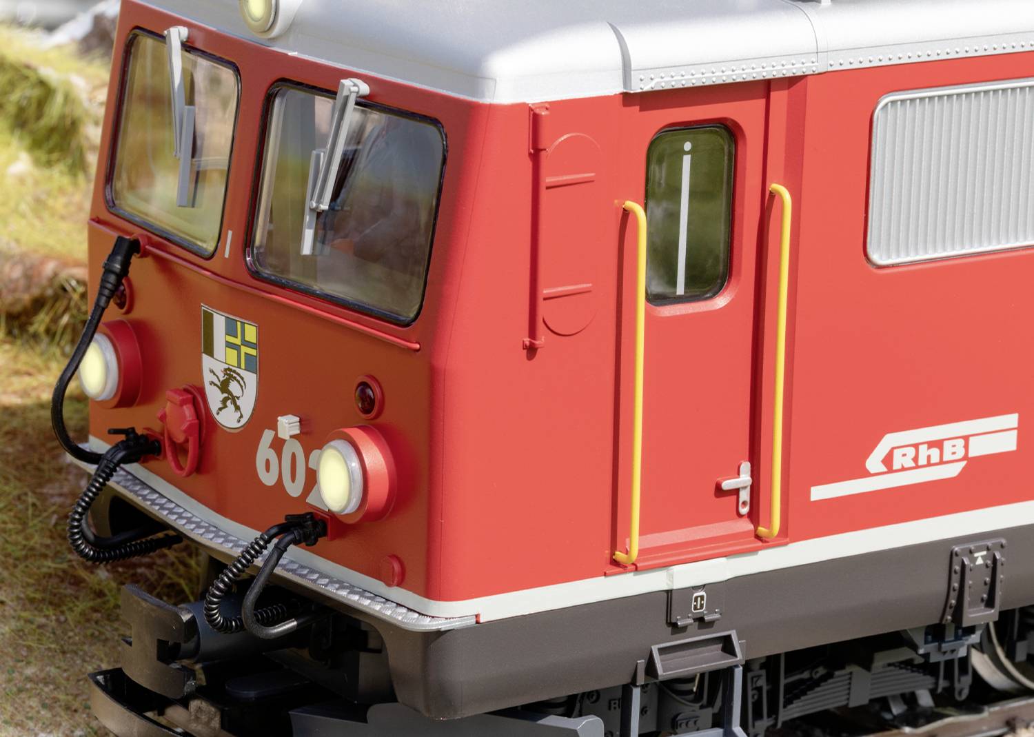 Ein roter Zug mit der Aufschrift 'RhB' und der Zahl '60' auf einem Gleis, detaillierte Modellbahnlandschaft im Hintergrund.