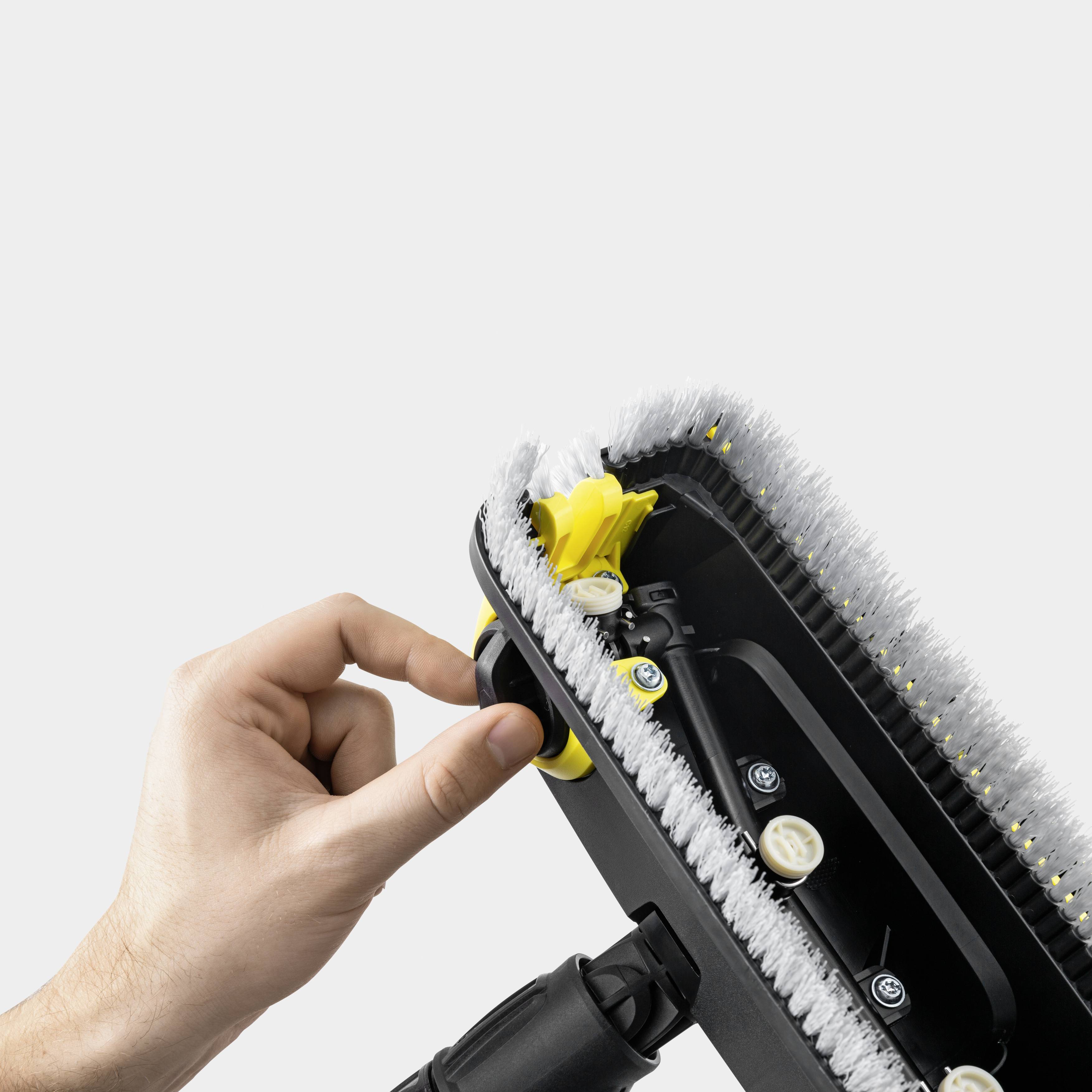 Eine Hand hält ein Bodenreinigungsgerät mit Sicht auf die Unterseite, das mehrere rotierende Bürsten und gelbe Zahnräder zeigt.