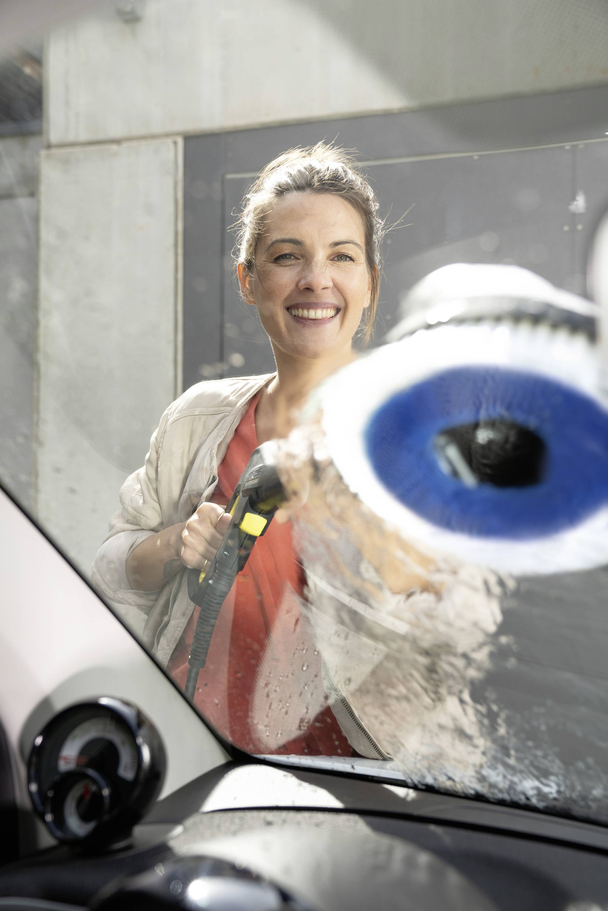 Eine Person wischt ein Autofenster von innen. Sie lächelt und verwendet ein blaues Reinigungswerkzeug.