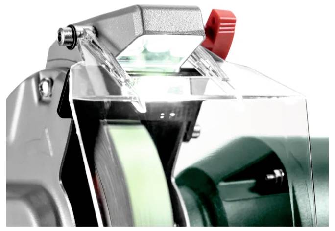 Eine Nahaufnahme einer Schleifmaschine mit Fokus auf das Schleifrad und die Schutzvorrichtung, mit einem kleinen Licht und rotem Verstellknopf.