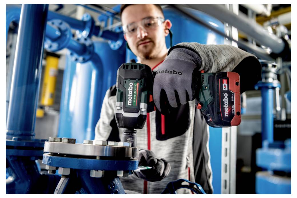 Eine Person, die mit einem Elektrowerkzeug an industrieller Maschinerie arbeitet und dabei Schutzhandschuhe und Schutzbrillen trägt, was Sicherheit und präzise Arbeitsweise signalisiert.