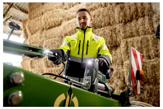 Mann in einer Warnweste, der eine grüne landwirtschaftliche Maschine in einer Heuscheune bedient.