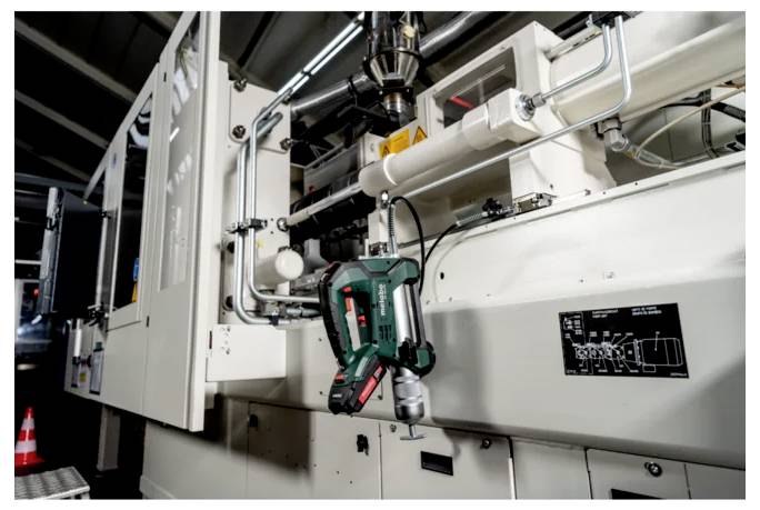 Industrielle Maschine mit einem grünen kabellosen Bohrer, der an einer robotischen Vorrichtung an einer Fabrikproduktionslinie befestigt ist.